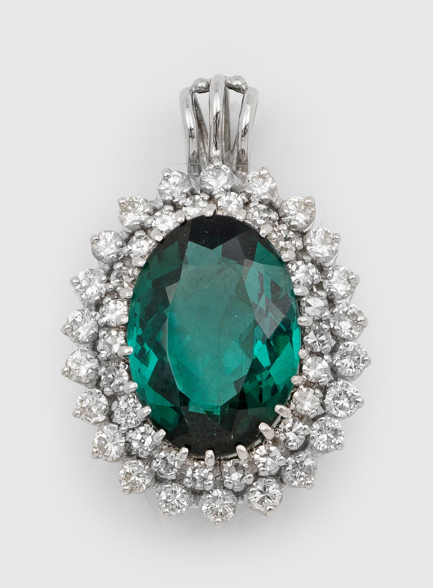 Klassischer Turmalin-Brillant-Anhänger: Weißgold, 14 ct.; Zentral besetzt mit einem petrolgrünen Turmalin von ca. 16 x 11 x 8 mm, entouriert von Brillanten von zus. ca. 1,00 ct.; Gew. ca. 8,00 g. Pendant set with a bottle green tourmaline