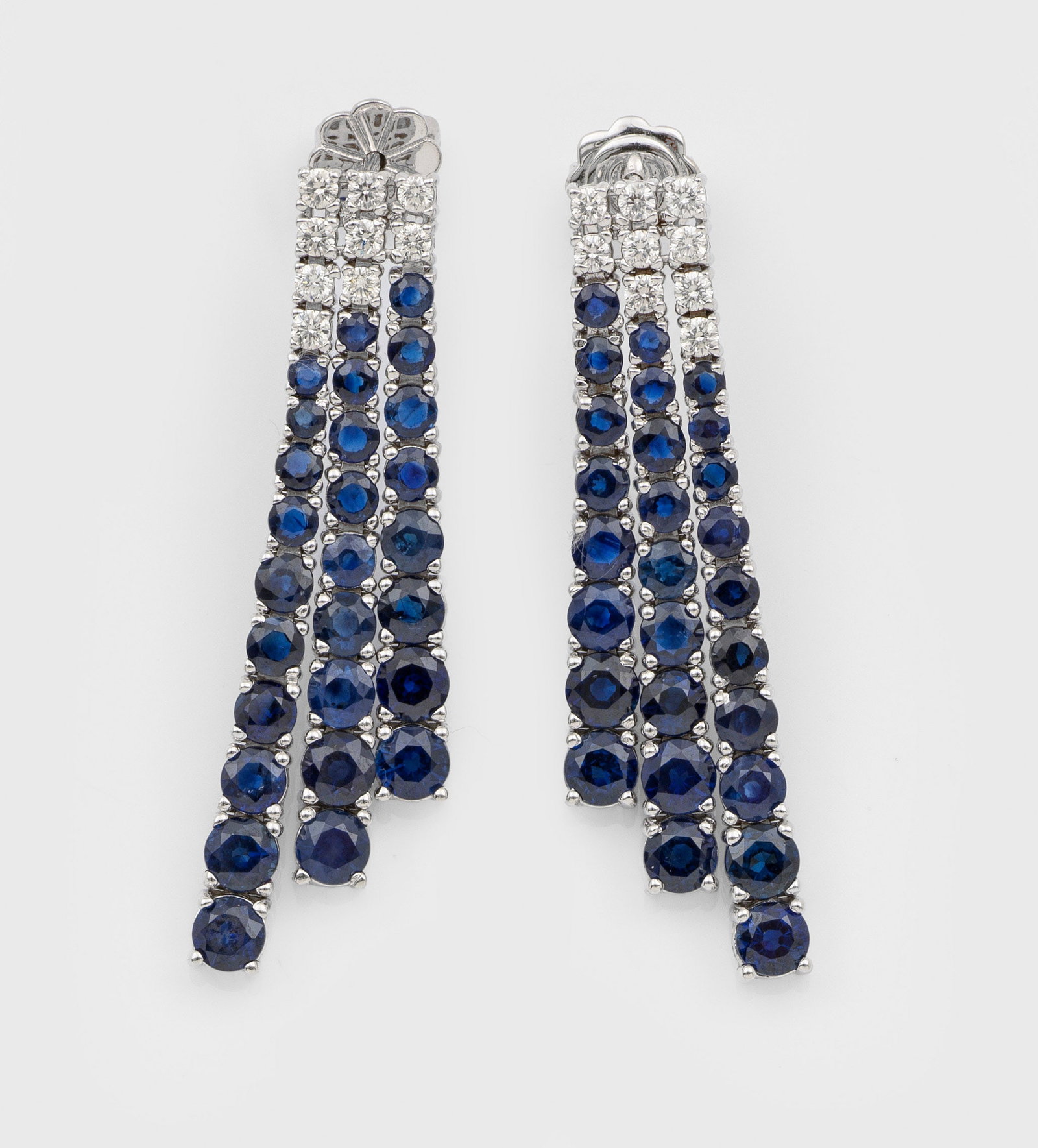 Paar elegante Saphir-Brillant-Ohrgehänge: Weißgold, gest. 750. Dreigliedrig linear besetzt mit tintenblauen Saphiren zus. ca. 10,11 ct. und zentral gesetzte Brillanten zus. ca. 0,58 ct.; Gew. ca. 11,90 g. Pair of earrings set with sapphires 