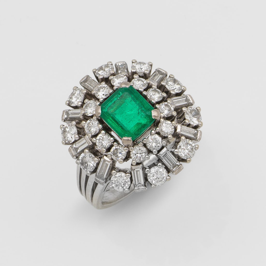 Cocktail-Diamantring mit kolumbianischem Smaragd: Weißgold, gest. 750. Zentral besetzt mit einem leuchtendgrünen Smaragd von ca. 1,50 ct. im Carréeschliff, in gestufter Anordnung umrahmt von Diamant-Baguetten und Brillanten von zus. ca. 2,00 ct. (