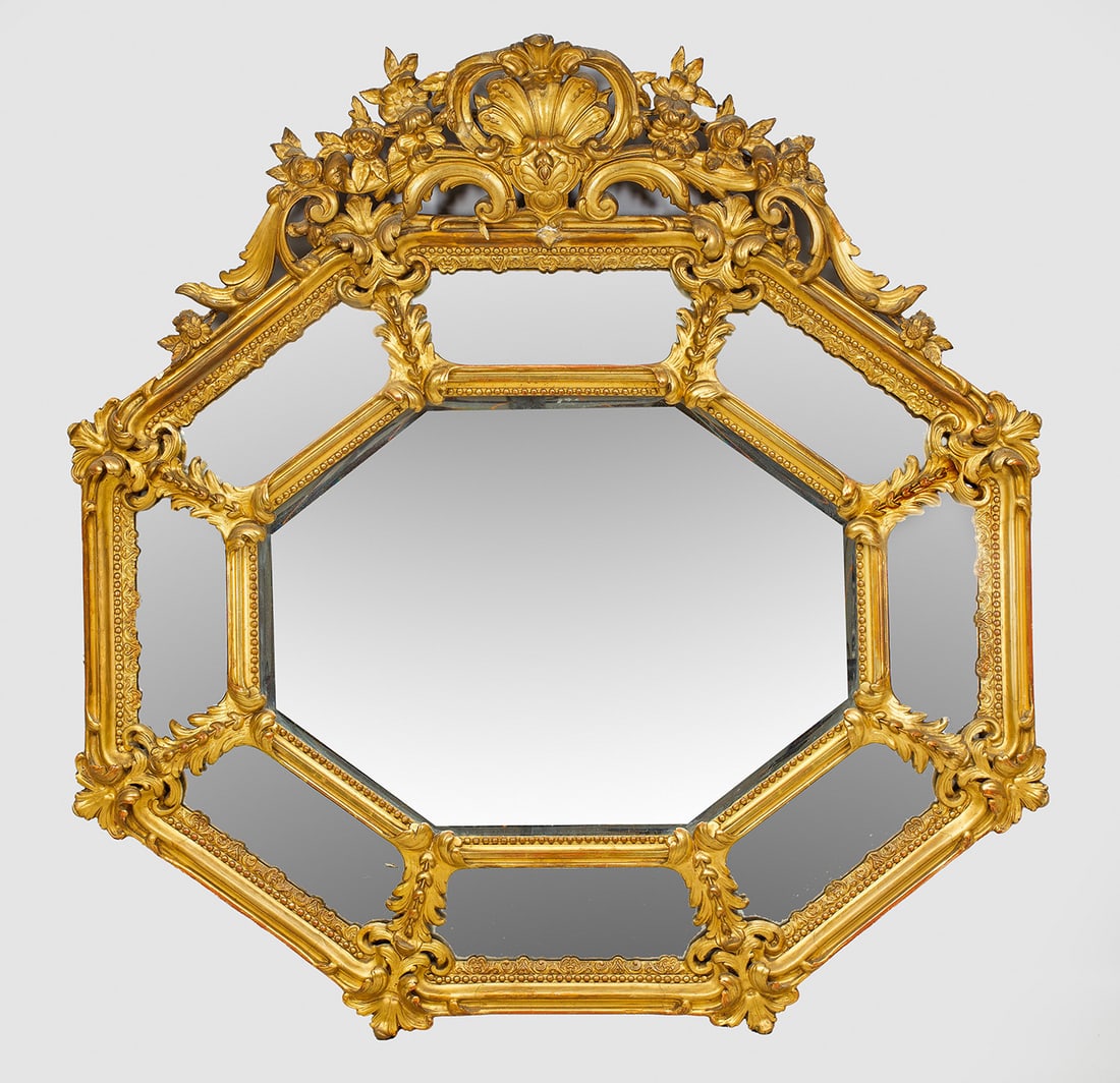 Großer Wandspiegel im Barock-Stil: Stuckiert und vergoldet. Querrechteckig oktogonale, kissenartig angelegte Spiegelrahmung aus schmalen Stegen, durch Blattwerk verbunden. Vorkragende Spiegelrahmung mit zentralem Muschelmotiv, umgeben 