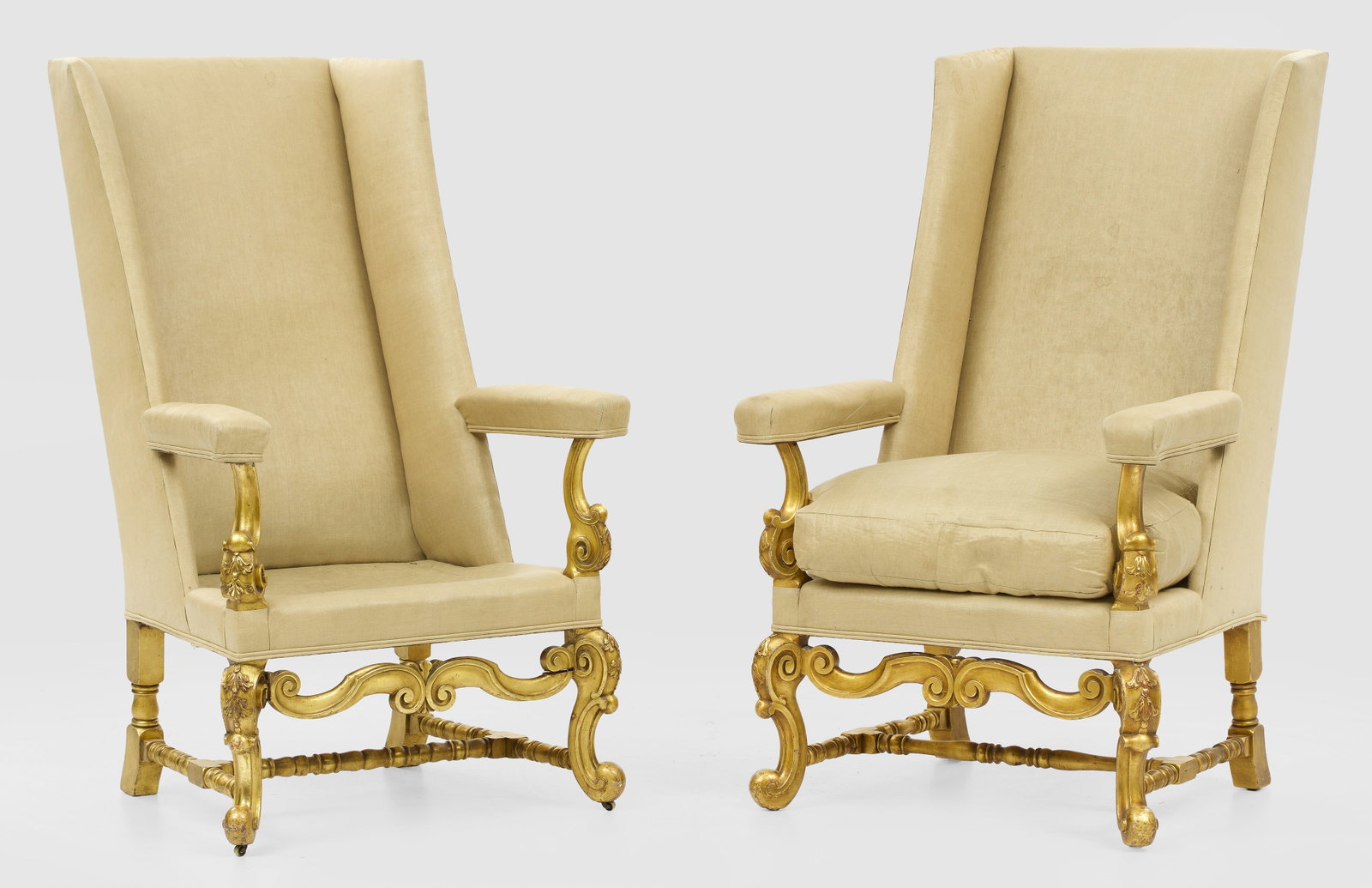 Paar große Kaminsessel im Barock-Stil: sog. Highback-Chairs. Holz, geschnitzt, gefasst und vergoldet. Trapezförmige Zarge auf geschwungenen Volutenbeinen, unterhalb durch Balusterstäbe verbunden. Korrespondierende Stützen für breite Ar