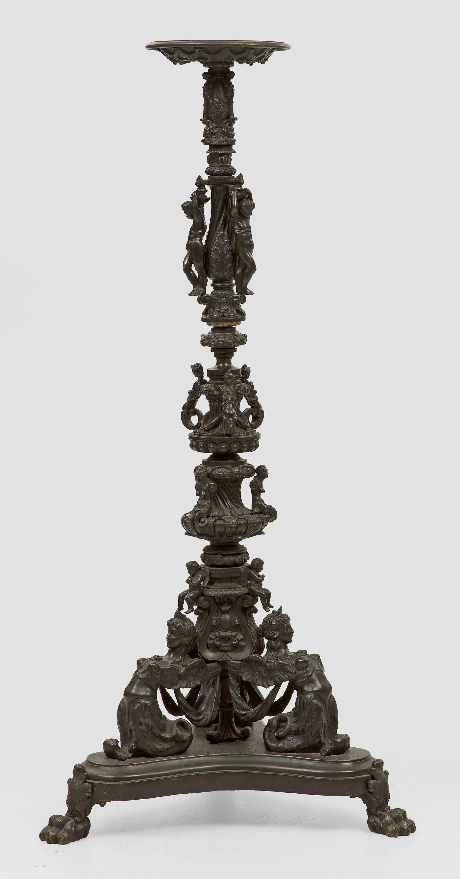 Napoleon III-Torchère: Bronze, dunkel patiniert. Über dreiseitig konkav eingezogener, profilierter Basis auf Tatzenfüßen vollplastisch gestaltete Genien als Träger für gestreckten, mehrfach gegliederten und blattrelief