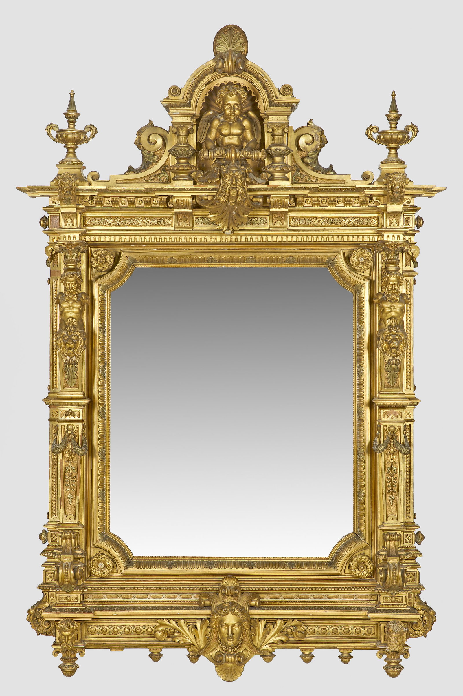 Höfischer Neorenaissance-Wandspiegel: Holz, geschnitzt, gefasst und vergoldet. Gerade, hochrechteckige, architektonisch gestaltete Spiegelrahmung, flankiert von gekanteten, blattreliefierten Pilastern mit männlichen Genien und Löwenmask