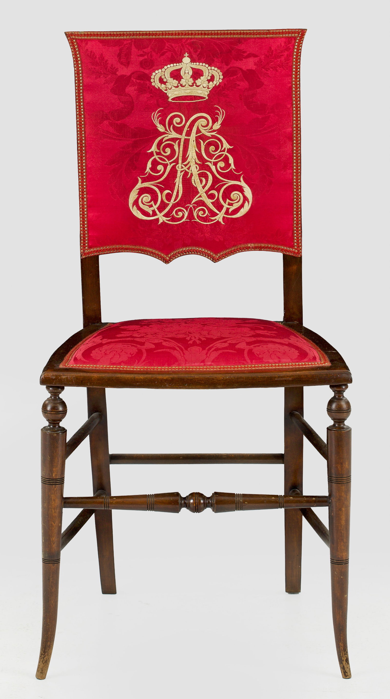 Höfischer Festsaal-Stuhl: aus dem Besitz von Prinz Alfons von Bayern Nussbaum. Trapezförmige, flache Sitzfläche auf spitz zulaufenden Rundbeinen, durch schmale Stege verbunden. Rechteckige, leicht ausschwingende Rückenlehne