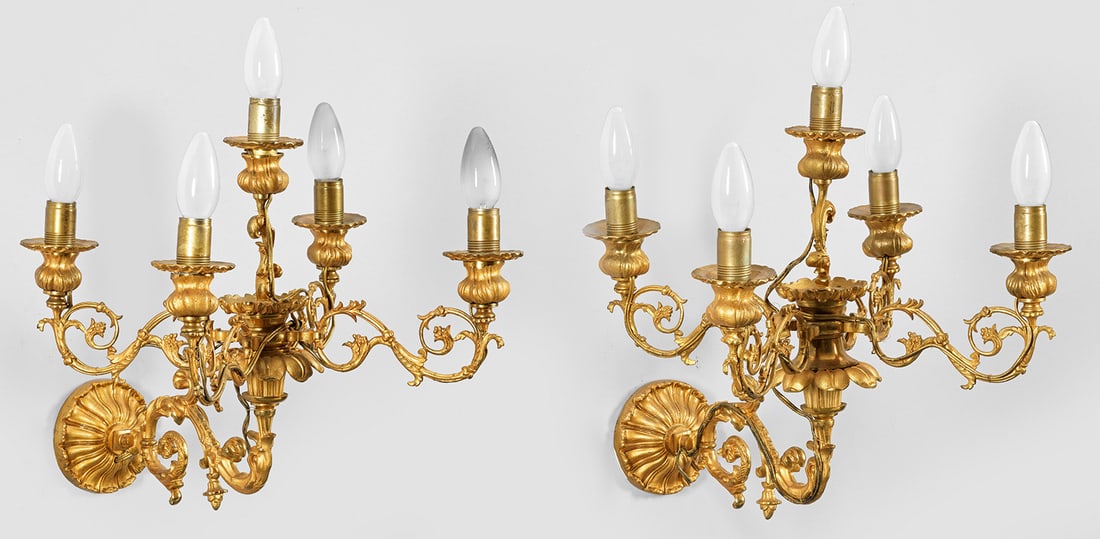 Paar Napoleon III-Wandgirandolen: 5-flg.; Bronze, vergoldet. Rosettenförmiges Wandschild. Mittig davon ausgehend stark geschwungener Leuchterarm mit stilisiertem Delfin. Oberhalb korrespondierendes Girandolenelement aus eingerollten 