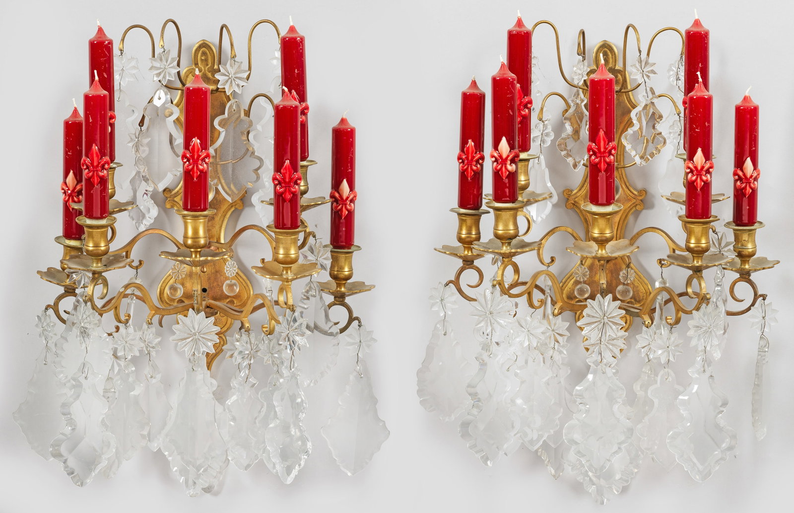Paar Wandgirandolen: 7-flg: Messing und farbloses Kristallglas. Flaches, balusterförmiges Wandschild. Davon ausgehend stark geschwungene Leuchterarme mit vasenförmigen Tüllen. Reicher Behang aus großen, facettierten P