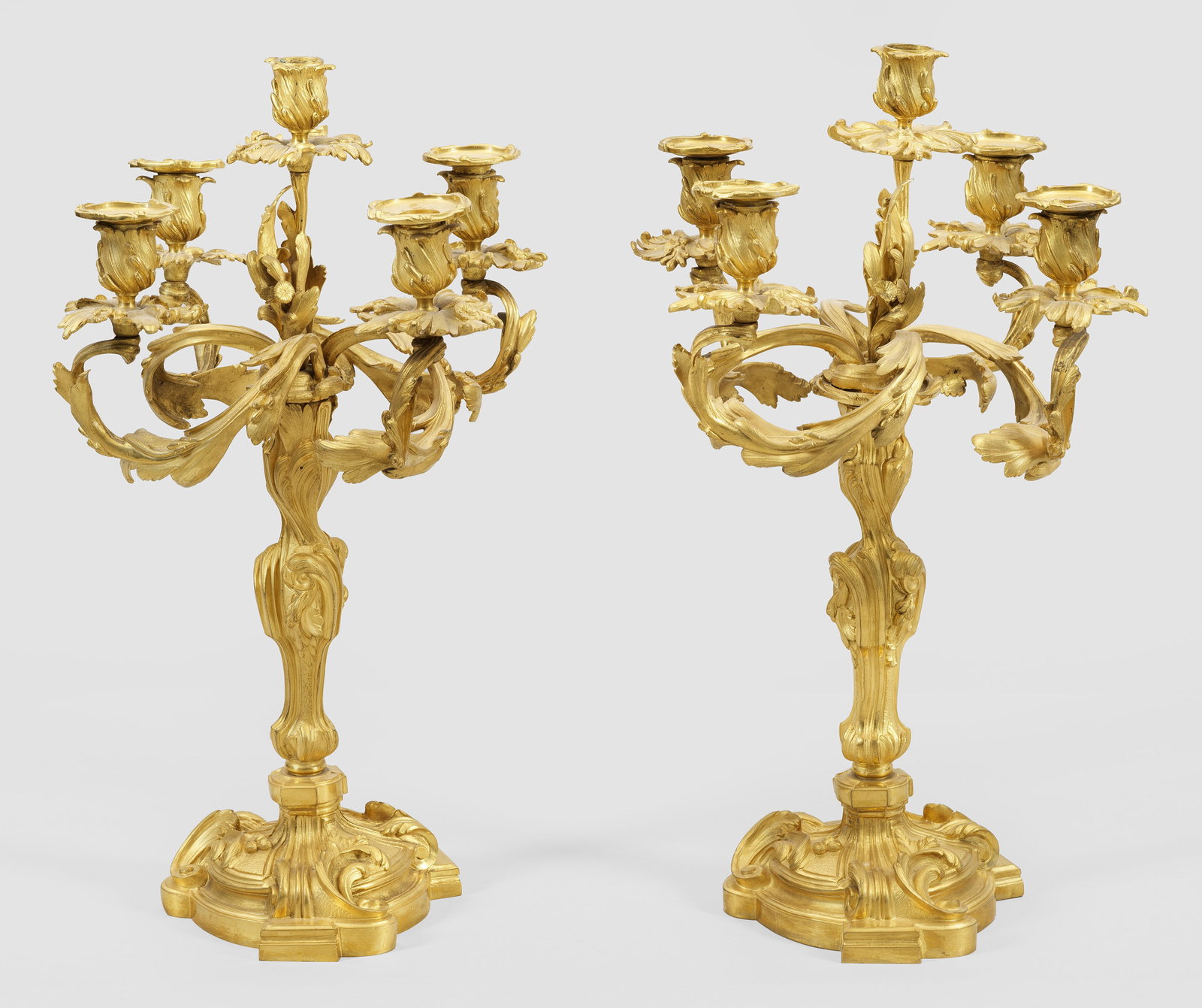 Paar Napoleon III-Prunkgirandolen: 1- bzw. 5-flg.; Bronze, vergoldet. Über geschweift ansteigender Basis balusterförmiger Rocailleschaft. Oberhalb abnehmbarer Girandolenaufsatz aus stark geschwungenen, blattreliefierten Leuchterarmen