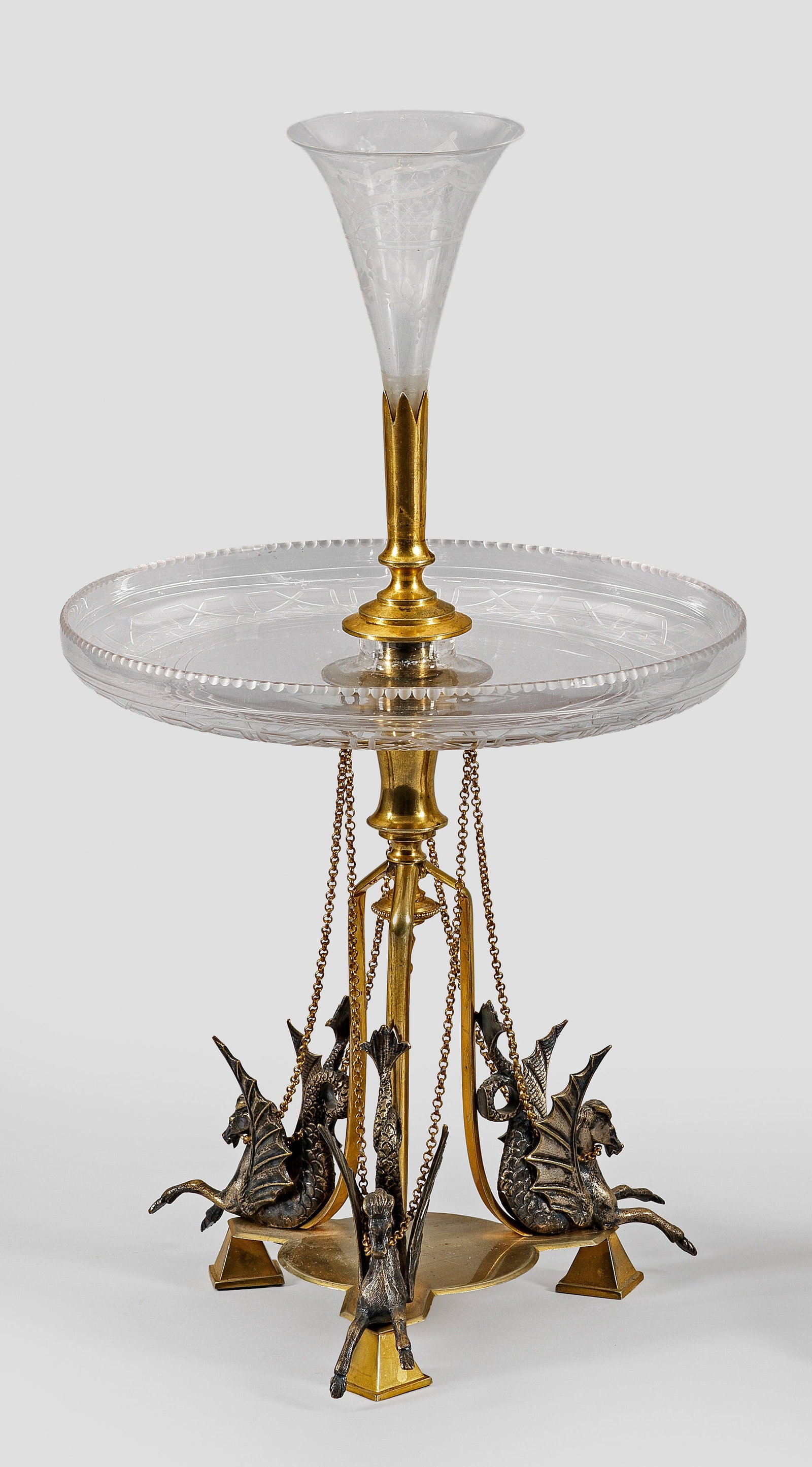 Napoleon III-Tafelaufsatz: Glas und Messing. Dreipassiger Fuß mit drei vollplastisch ausgearbeiteten Hippokampen. Über kurzem Balusterschaft runder Glasteller mit aufgewölbtem Rand, verschraubt mit Messingtülle, in der die 