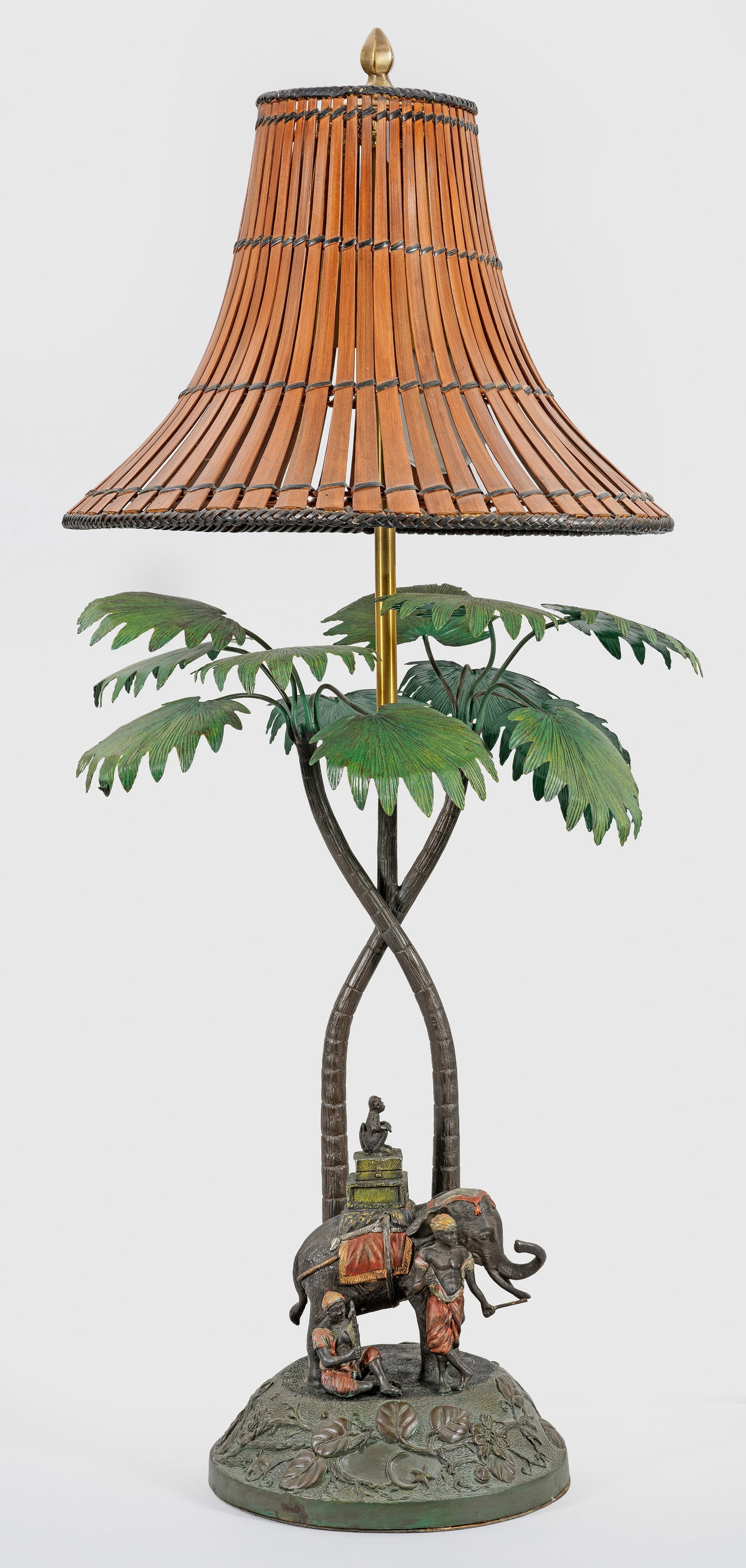 Exotische Tischlampe im Stil der Wiener Bronzen: 2-flg.; Bronze dunkel patiniert und farbig staffiert. Über sich konisch verjüngenden Sockel mit umlaufendem Blattfries skulpturale Darstellung mit einem Elefanten. Dahinter gestreckte Streben in For