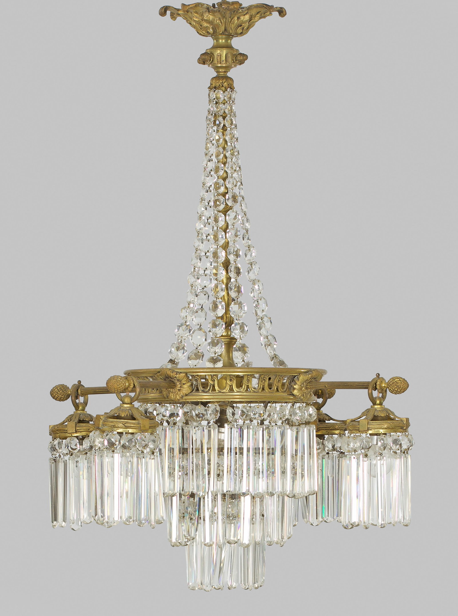 Belle Epoque-Deckenlüster: 4-flg.; Bronze und farbloses Glas. Balusterförmiger Korpus aus Prismenschnüren im Verlauf sowie gestaffelt angeordneten Prismenstäbchen. Durchbrochen gearbeiteter, konkav eingezogener Reif. Davon a