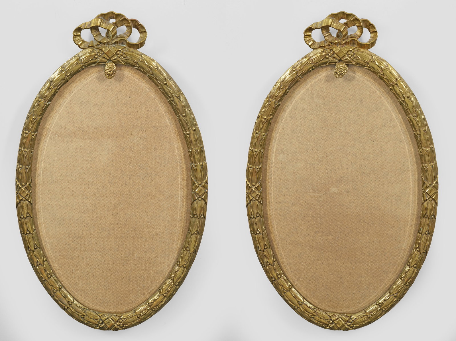Paar Rahmen im Louis XVI-Stil: Bronze. Hochovale Spiegelrahmung mit umlaufendem Fries aus Lorbeerblatt sowie durchbrochen gearbeiteter Schleifenbekrönung. Facettiertes Glas. 71 cm x 42 cm. A pair of French bronze Louis XVI style f