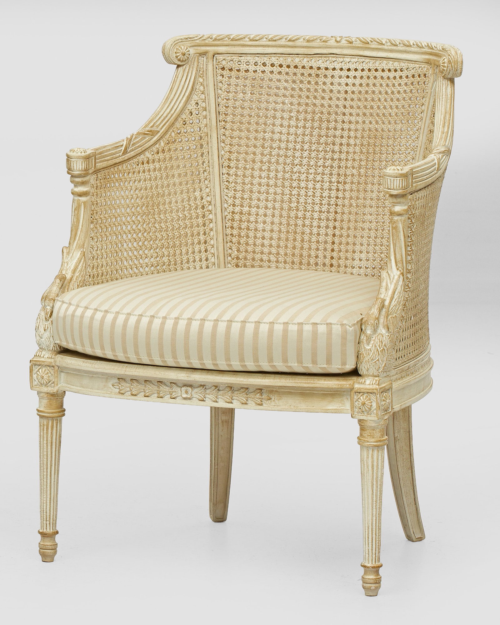 Bergère im Louis XVI-Stil: Holz geschnitzt und cremefarben gefasst. Bombierte Zarge auf kannelierten Balusterbeinen. Plastisch gestaltete Stützen aus Schwänen für geschweift ansteigende, schmale Armlehnen. Gewölbte