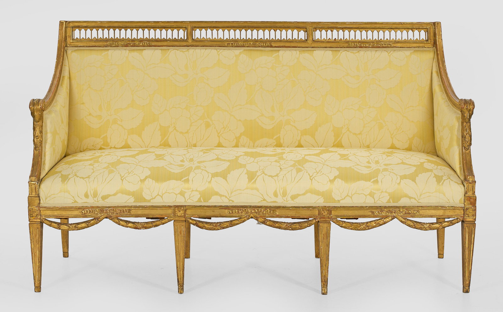 Großes Louis XVI-Canapé: Holz, geschnitzt, gefasst und vergoldet. Schmale, profilierte Zarge auf konischen Vierkantbeinen, unterhalb durch plastische Maskarons verbunden. Geschweift ansteigende Streben als Stützen für schma