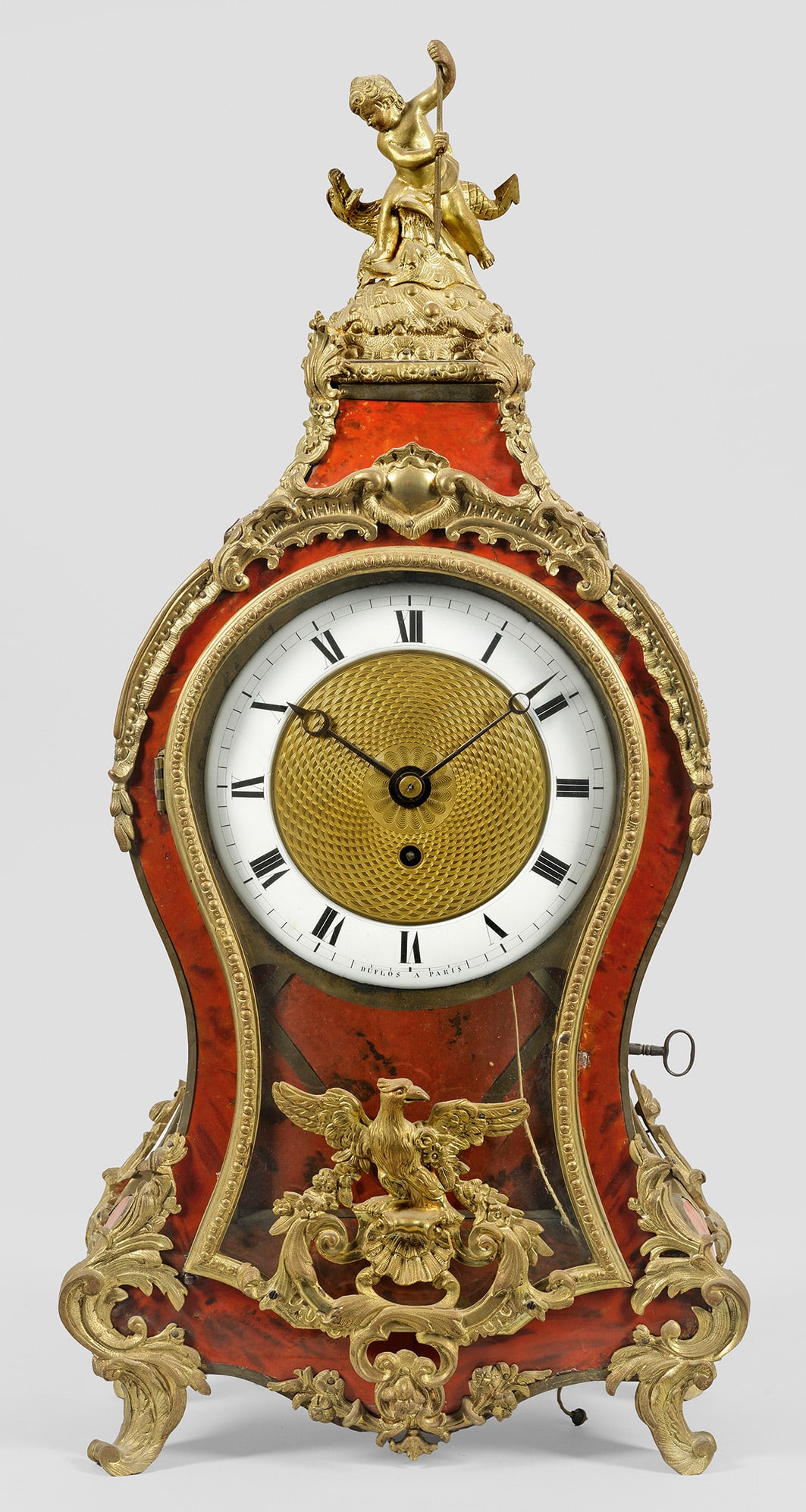 Pendule im Louis XV-Stil: Flächendeckender Fond aus rothinterlegtem Lack und Bronze. Balusterförmiger, dreiseitig verglaster Korpus, flankiert von Rocaillen und Blattvoluten mit geschweift ansteigendem oberen Abschluss und P