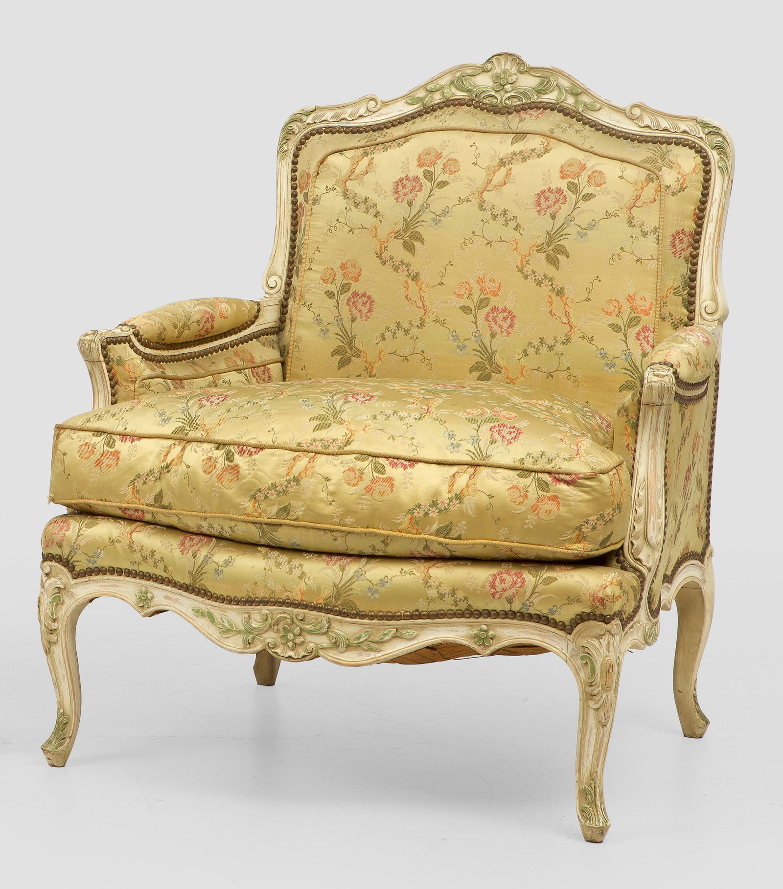 Große Bergère im Louis XV-Stil: Holz, reliefplastisch geschnitzt, cremefarben gefasst und teilw. grün akzentuiert. Passig geschweifte, blattreliefierte Zarge auf geschwungenen Beinen. Korrespondierende Stütze für schmale Armlehne
