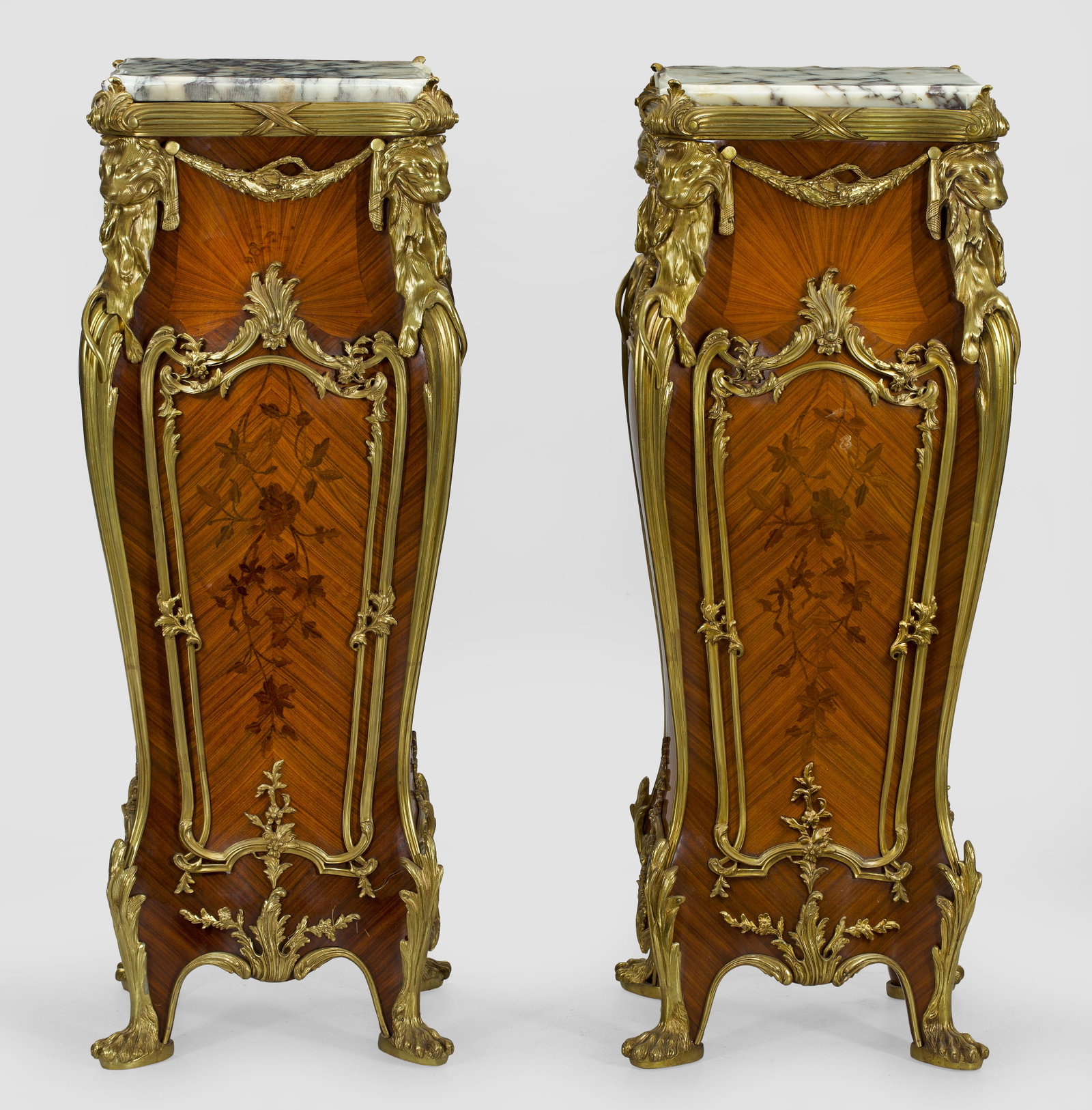 Paar große repräsentative Podestsockel im Louis XV-Stil: Nussbaum und Rosenholz, furniert sowie reiche Applikationen aus Bronze. Balusterförmiger, bombierter Korpus, flankiert von ausgezogenen Ecklisenen mit plastischen Löwenmaskarons. Profilgerahmte