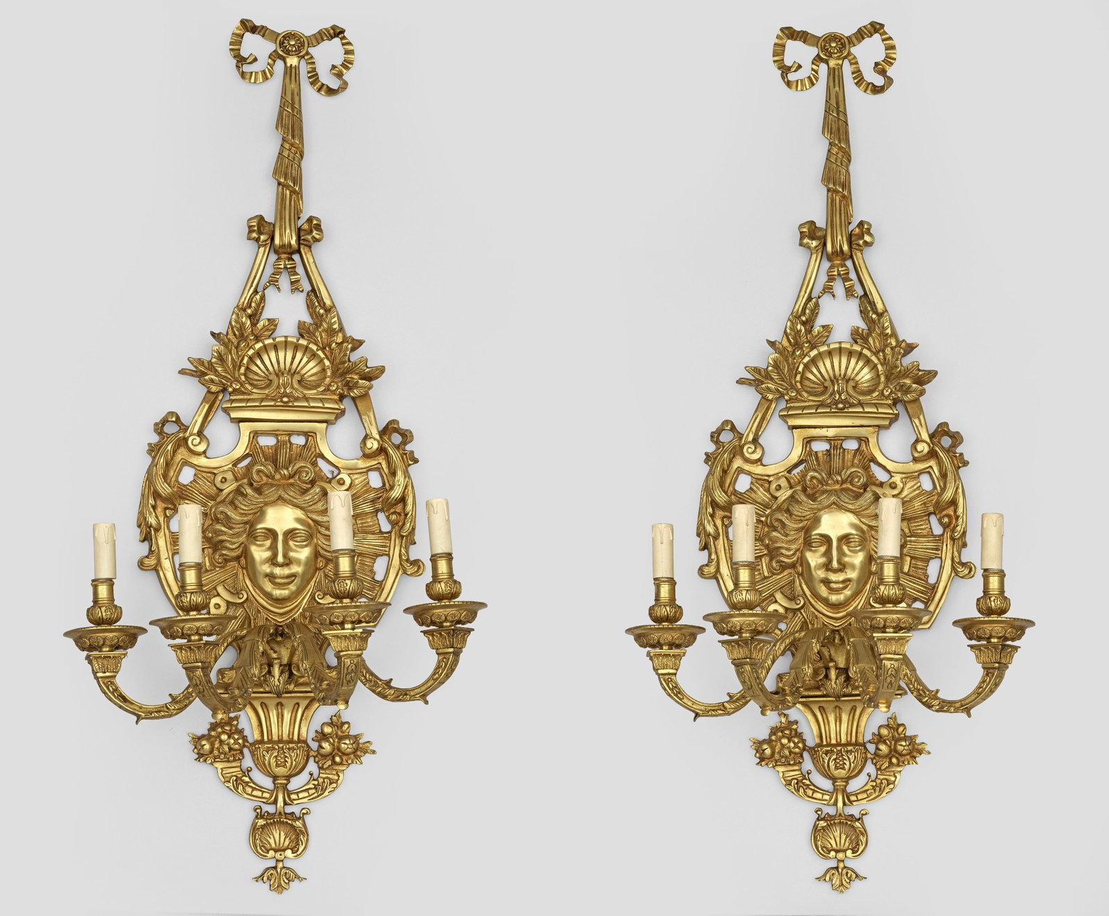 Paar große Wandappliken im Louis XIV-Stil: 4-flg.; Bronze. Balusterförmiger Wandschild mit großem, erhaben reliefiertem Maskaron, umgeben von üppigen Voluten an schleifenbekröntem Draperiewerk. Unterhalb davon ausgehend stark geschwungene 