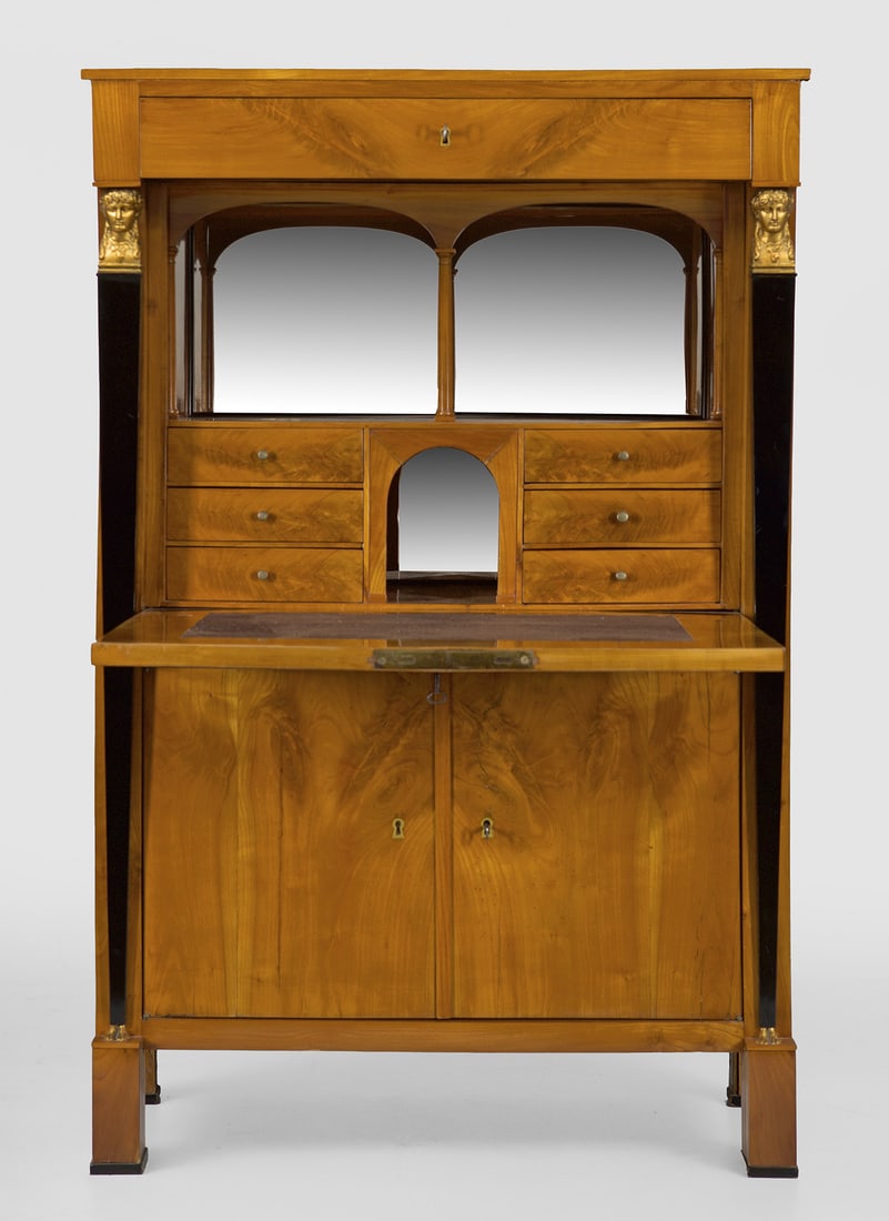 Biedermeier-Sekretär: Kirschbaum, furniert und teilw. ebonisiert. Gerader, hochrechteckiger Korpus, flankiert von eingestellten Karyatiden auf gekanteten Füßen. In der gegliederten Front breite Schublade, zwei Türen mit
