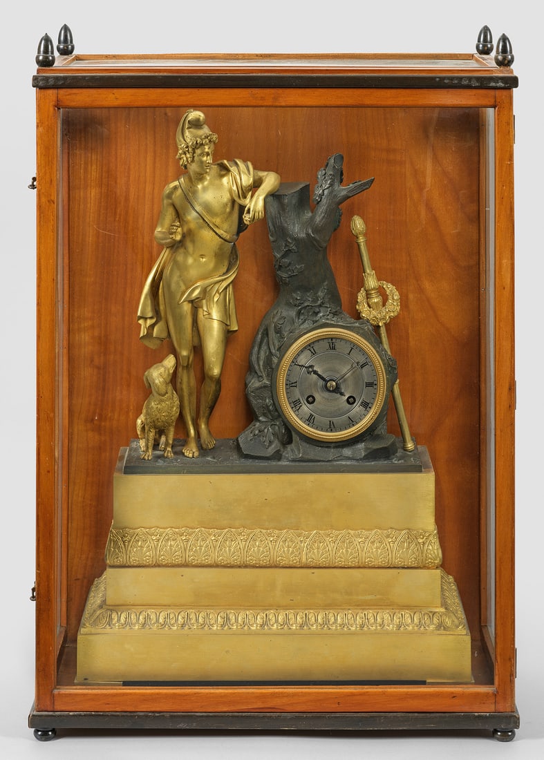Charles X-Pendule mit Schaukasten: Bronze, vergoldet und teilw. dunkel patiniert. Über hohem Sockel mit Palmettenfries naturalistisch gestaltetes Uhrengehäuse sowie vollplastische Darstellung des jungen Paris mit Apfel und einem Hund