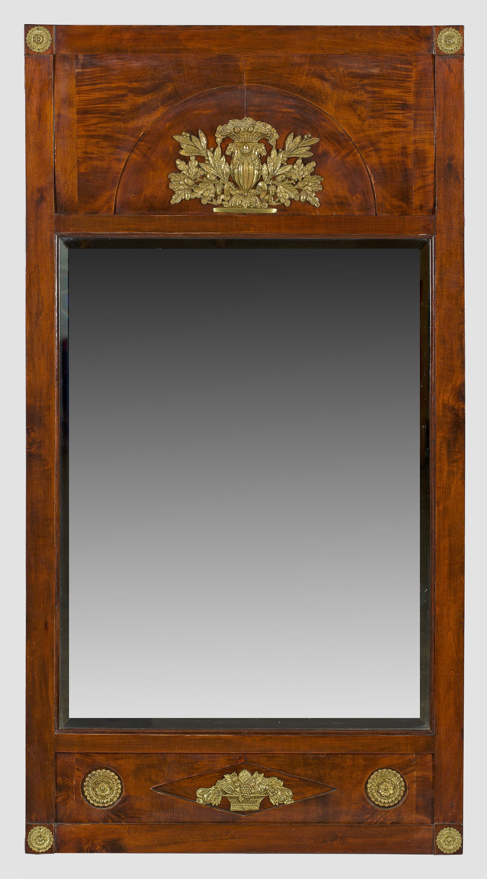 Biedermeier-Wandspiegel: Mahagoni, furniert sowie Applikationen aus Messing. Gerade, hochrechteckige Spiegelrahmung mit Rosettenmotiven auf den Ecken. Im breiten Giebelfeld leicht zurückgesetzter Segmentbogen mit applizierte