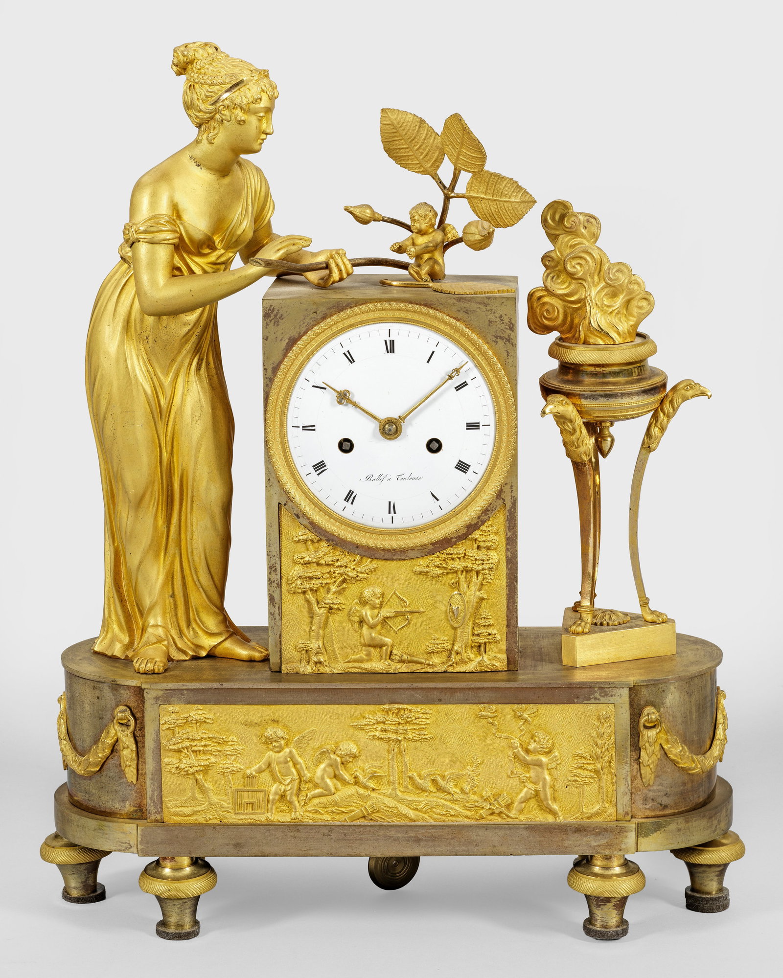 Empire-Figurenpendule: Bronze, vergoldet. Querrechteckig, seitlich gerundeter Sockel mit breitem, szenisch angelegtem Puttenfries auf Balusterfüßen. Oberhalb hochrechteckiges Uhrengehäuse sowie vollplastische Darstellung