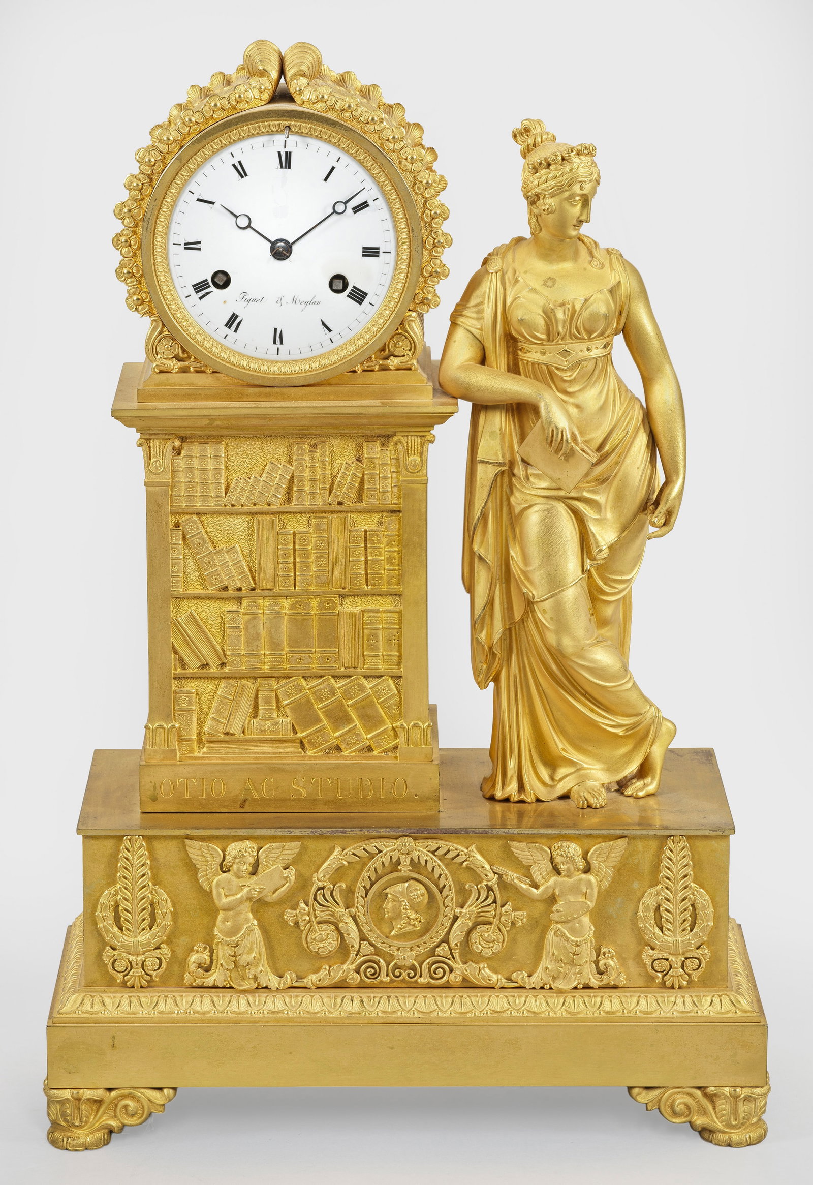 Empire-Figurenoendule "Otio ac Studio": Bronze, vergoldet. Über rechteckig angelegtem Sockel mit erhaben reliefierten Genien und Palmettenfries, vollplastische Darstellung einer jungen, antikisierend gekleideten Dame mit Buch, an das recht