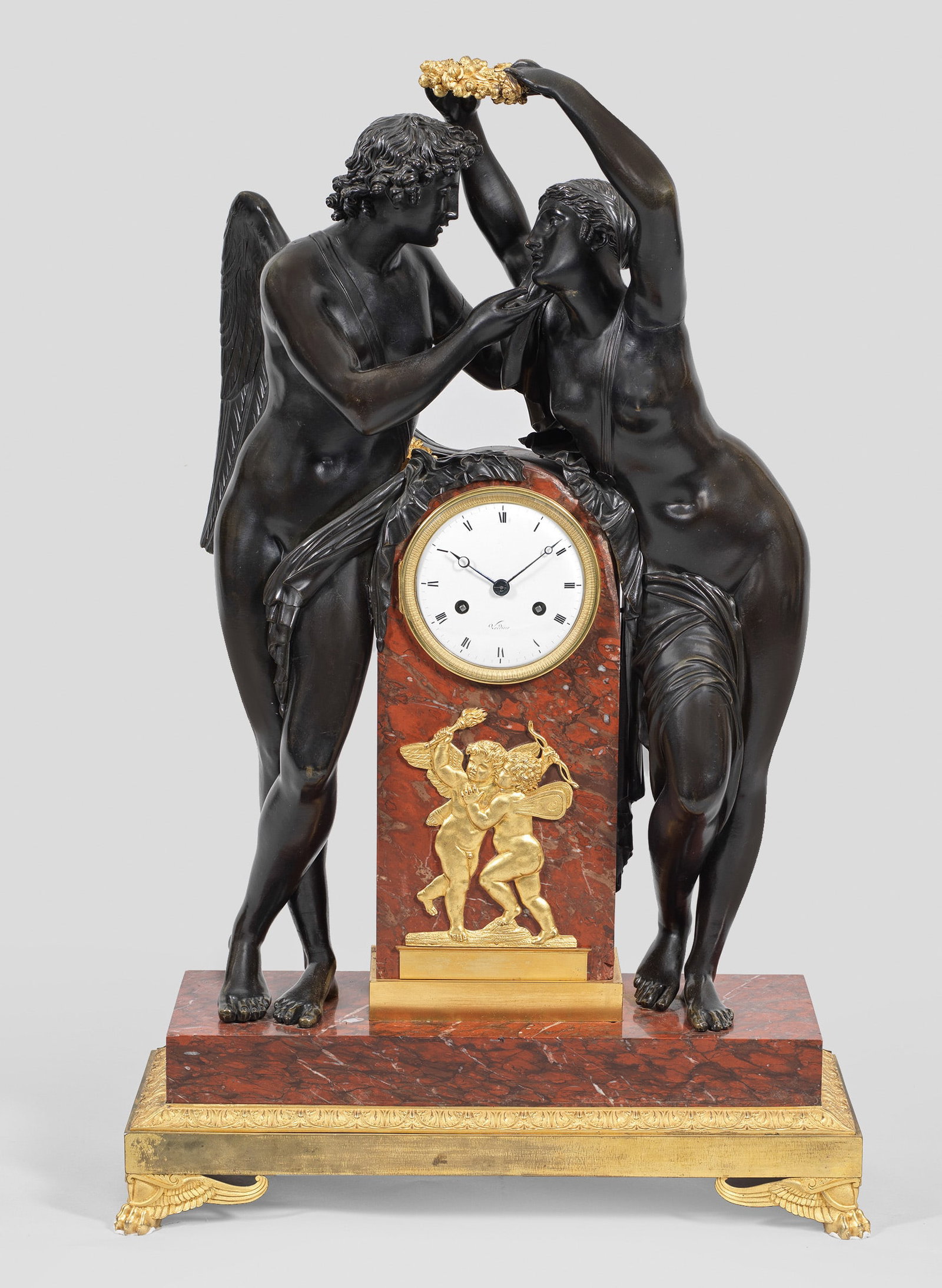 Große Empire-Figurenpendule "Amor und Psyche": nach einem Entwurf von Claude Michallon Bronze, dunkel patiniert und teilw. vergoldet sowie bordeauxroter, grau-weiß gemaserter Marmor. Vollplastische Darstellung von Amor und Psyche mit Kranz aus Ro
