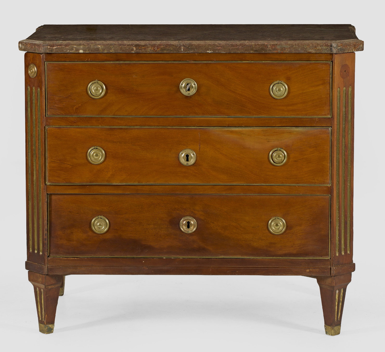 Louis XVI-Kommode: Mahagoni, furniert sowie Einlagen und Profile aus Messing. Rechteckig angelegter Korpus, flankiert von schräggestellten, kannelierten Ecklisenen auf konischen Vierkantbeinen. In der gegliederten Fron