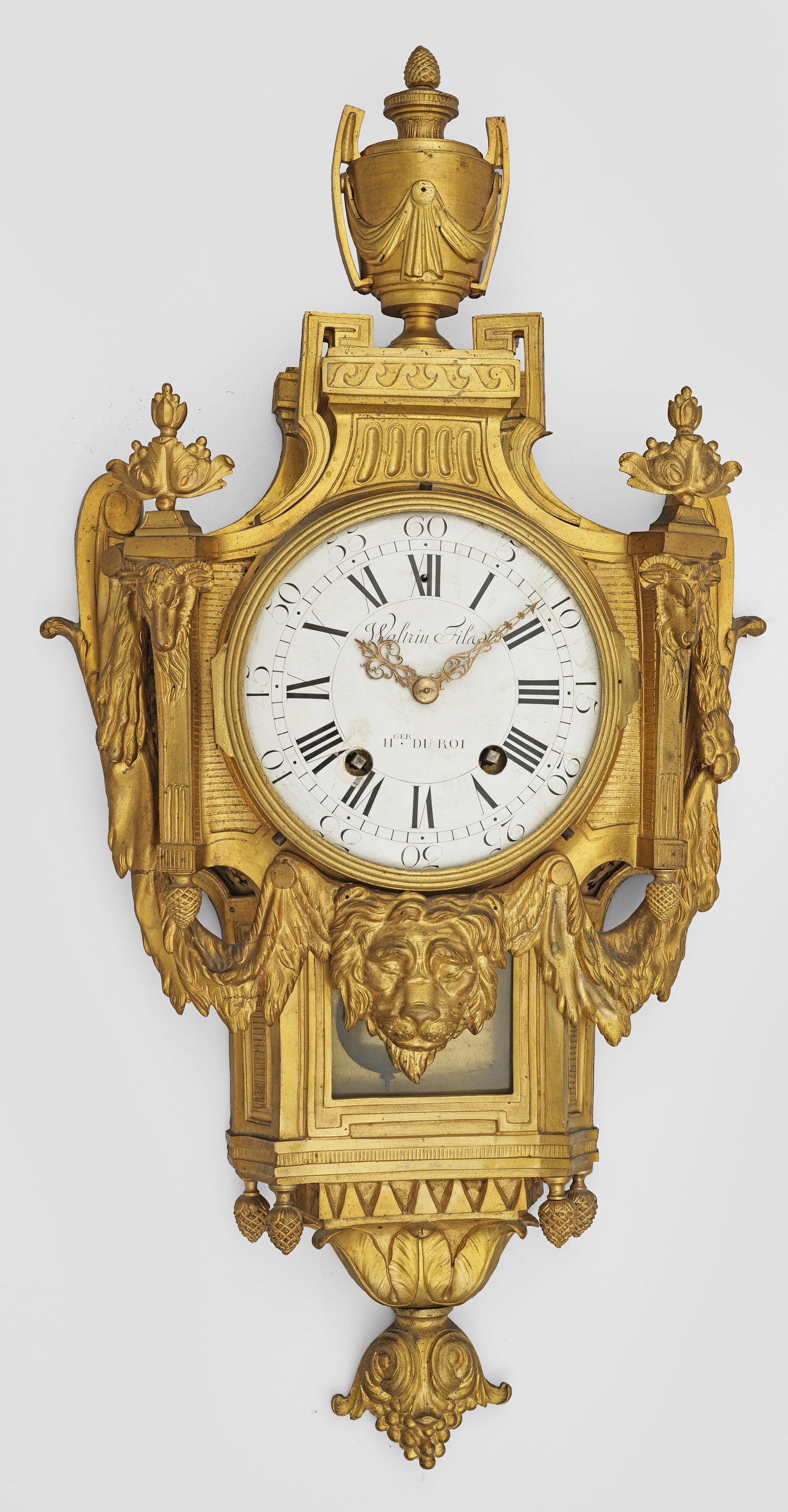 Große Louis XVI-Carteluhr: Bronze, vergoldet. Balusterförmiger, durchbrochen gearbeiteter Korpus, flankiert von blattbekrönten Pilastern mit reliefplastischen Widderköpfen, umgeben von üppigen Festons mit Löwenmaskaron. Be