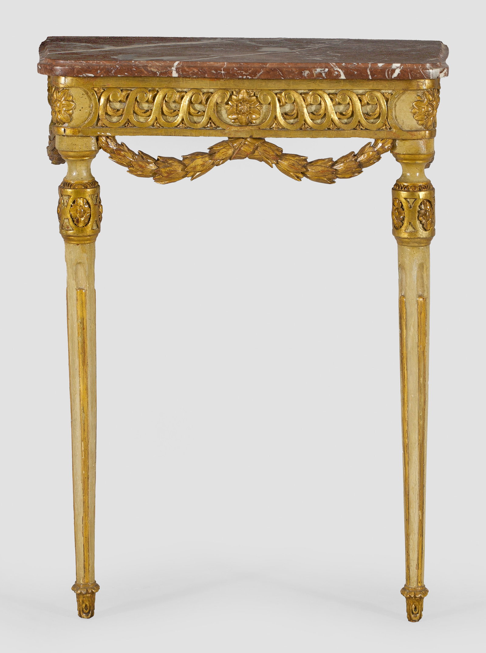 Louis XVI-Konsole: Holz, geschnitzt, cremefarben gefasst und teilw. vergoldet. Schauseitig leicht bombierte Zarge mit Wellenbandfries sowie gerundeten Ecken mit Blütenrosetten auf kannelierten Balusterbeinen, durch pla