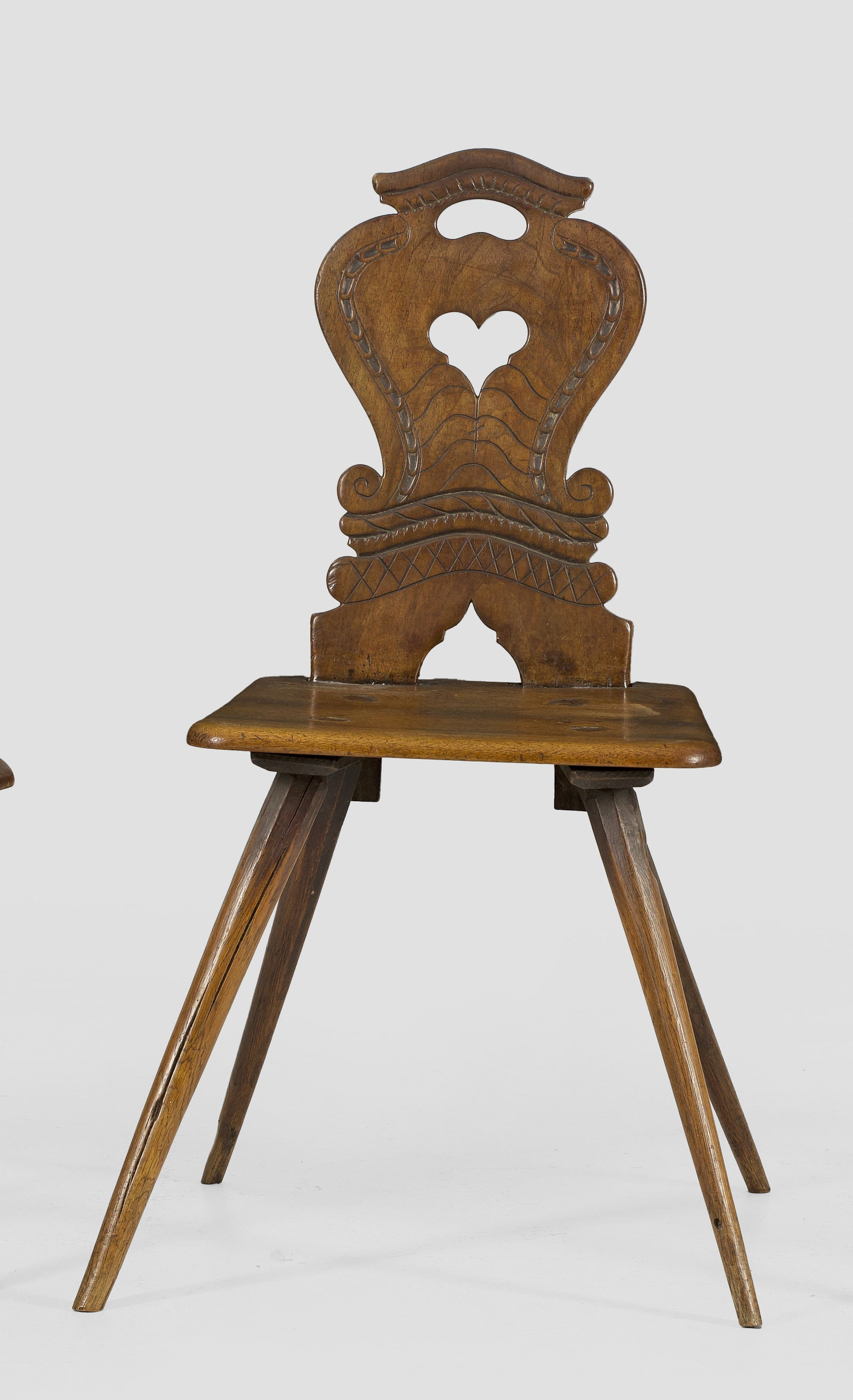 Brettstuhl: Nussbaum. Flache, gerundete Sitzfläche auf schräggestellten, gekanteten Beinen. Balusterförmige, herzförmig durchbrochen gearbeitete Rückenlehne. Sitz-H. 43 cm. Provenienz: Auflösung der Privats