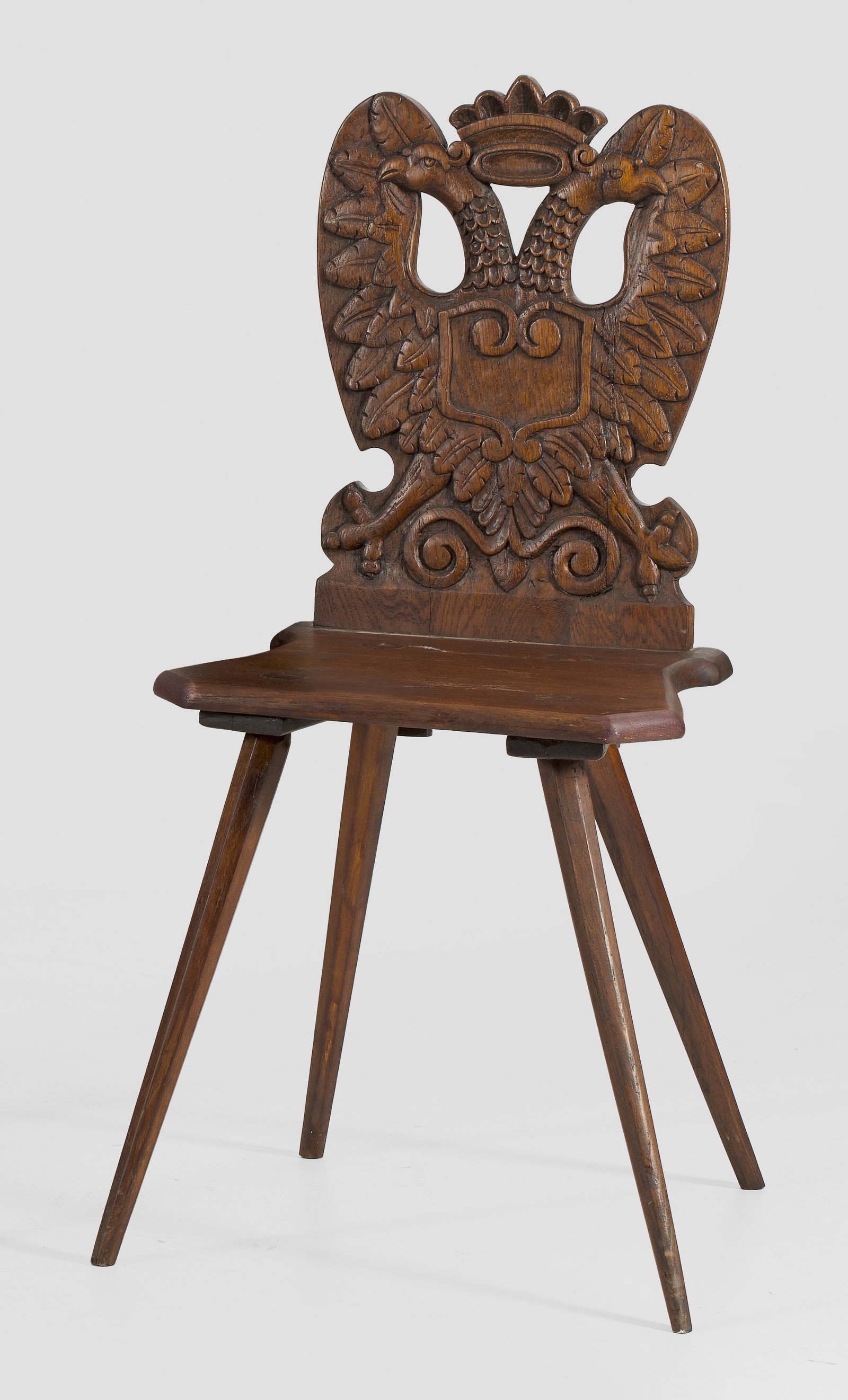 Brettstuhl: Eichenholz. Flache Sitzfläche auf schräggestellten, gekanteten Beinen. Balusterförmige, durchbrochen gearbeitete Rückenlehne mit erhaben reliefiertem Doppeladler. Sitz-H. 47 cm. A German oskwood c