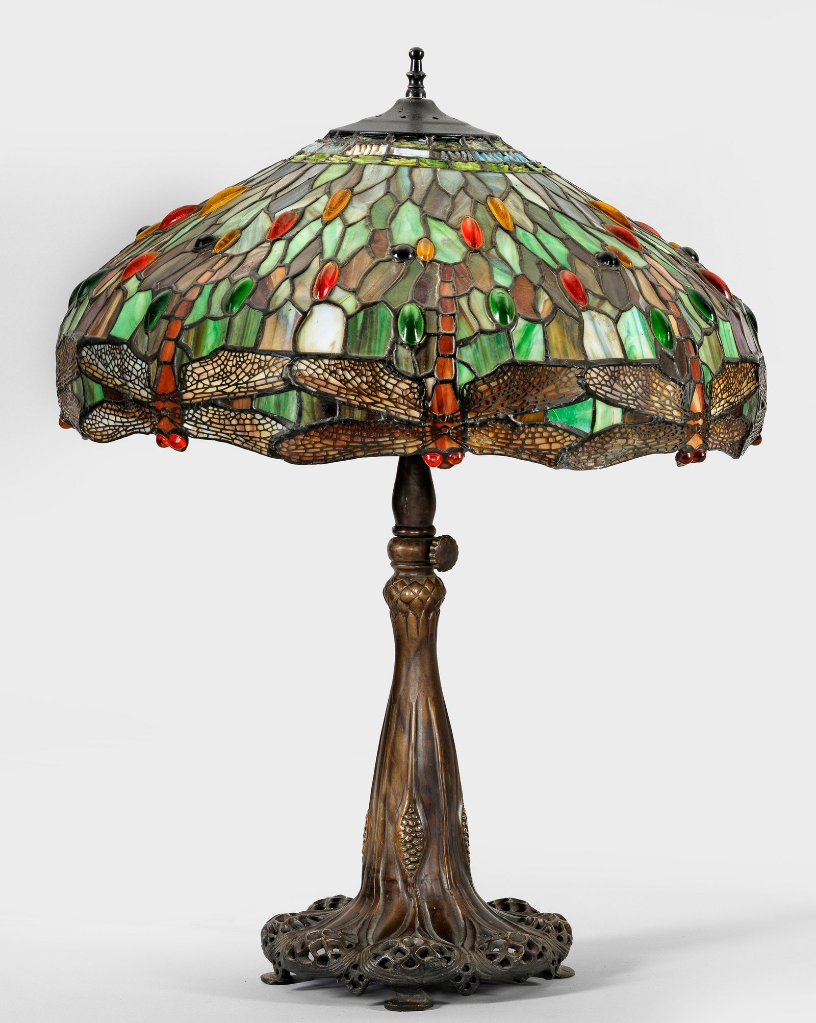 Große Tischlampe im Tiffany-Stil: 2-flg.; Bronze patiniert sowie farbiges Glas in unterschiedlichen Beige-, Braun- und Grüntönen sowie Rot. Geschweift ansteigender, durchbrochen gearbeiteter und vegetabil gestalteter Schaft als Trä