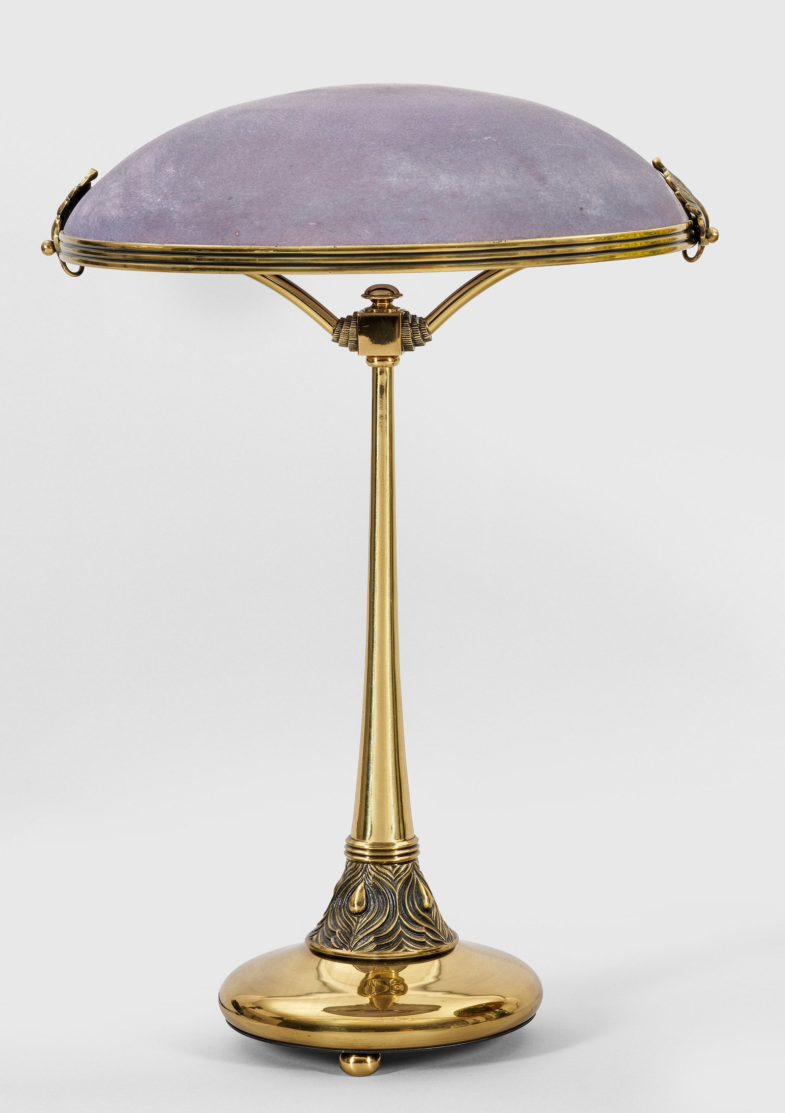 Tischlampe im Jugendstil: 2-flg.; Messing und violettes, satiniertes Glas. über geschweift ansteigender Basis sich konisch verjüngender, ornamental reliefierter Schaft. Davon ausgehend korrespondierende Streben als Träger f