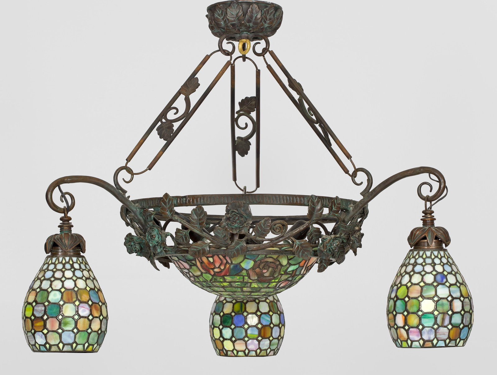 Große Deckenlampe im Jugendstil: 3-flg. Bronze, dunkel patiniert sowie farbiges Glas. Durchbrochen gearbeiteter Ring aus Rosenranken als Träger für kuppelförmigen Lampenschirm. Oberhalb gebogte Leuchterarme mit kelchförmigen Lamp