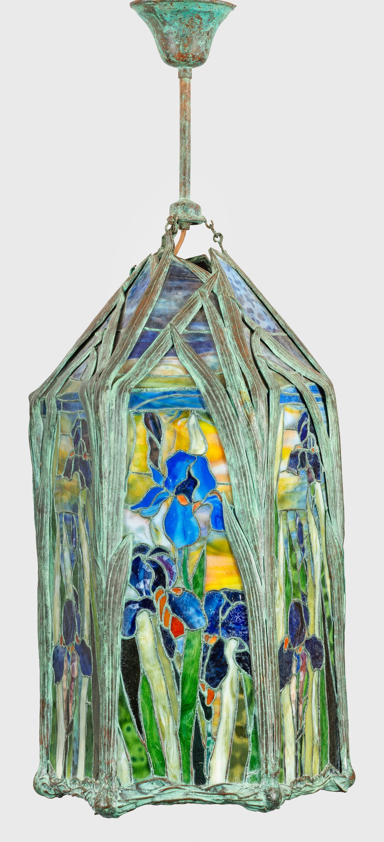 Deckenlampe im Tiffany-Stil: Bronze, grün patiniert sowie farbiges Glas in unterschiedlichen Grün-, Blau- und Orangetönen. Hoher, hexagonaler Korpus aus vegetabil gestalteten Streben in Form von reliefiertem Schilfblatt mit sc