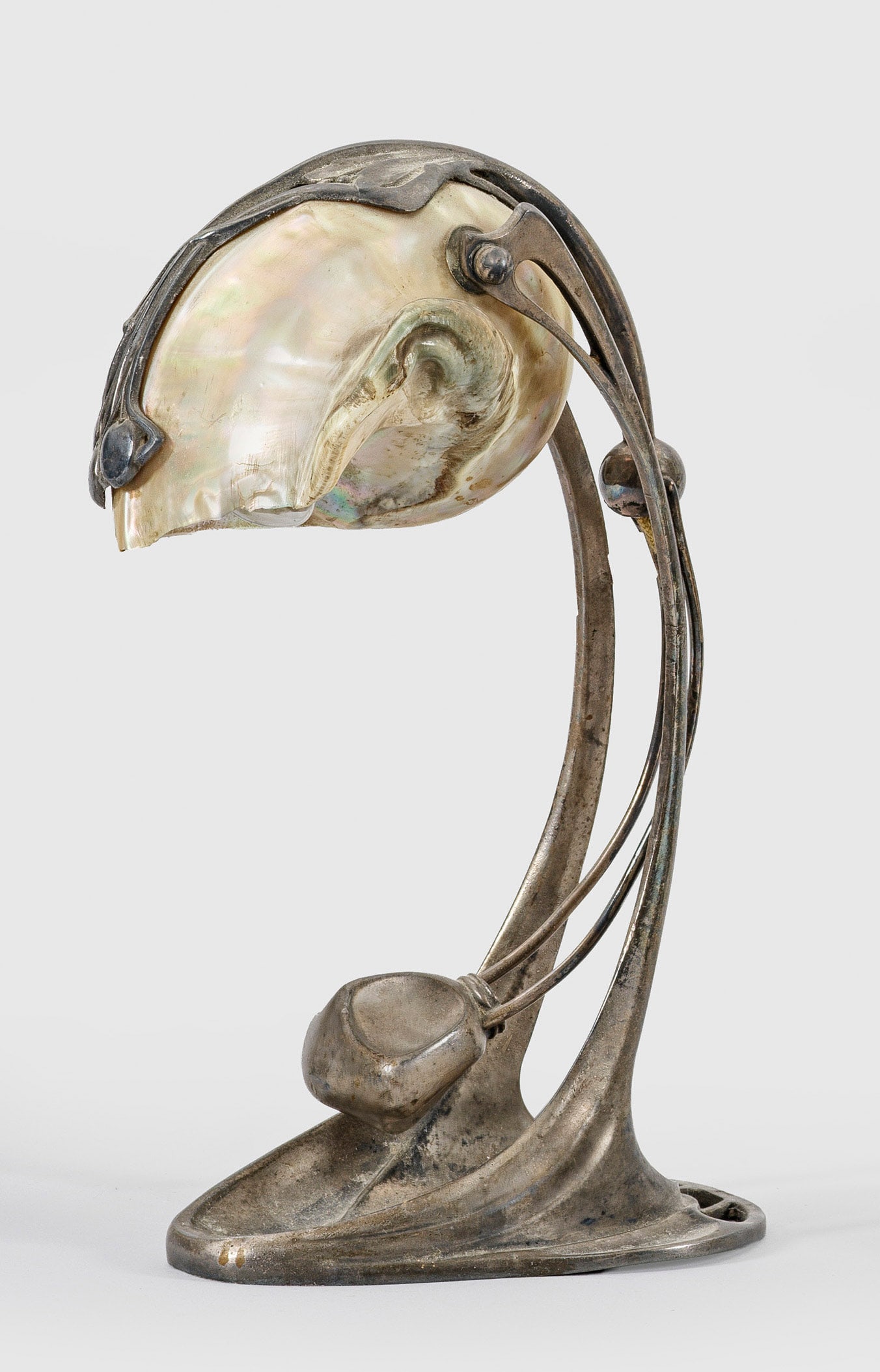 Jugendstil-Tischlampe von Moritz Hacker: 1-flg.; Metall, mit Resten von Versilberung und Gehäuse einer Nautilusmuschel. Vegetabil gestaltete Basis, in gebogte Streben übergehend. Dazwischen schwenkbares Leuchtmittel. Elektrifiziert. Besch.