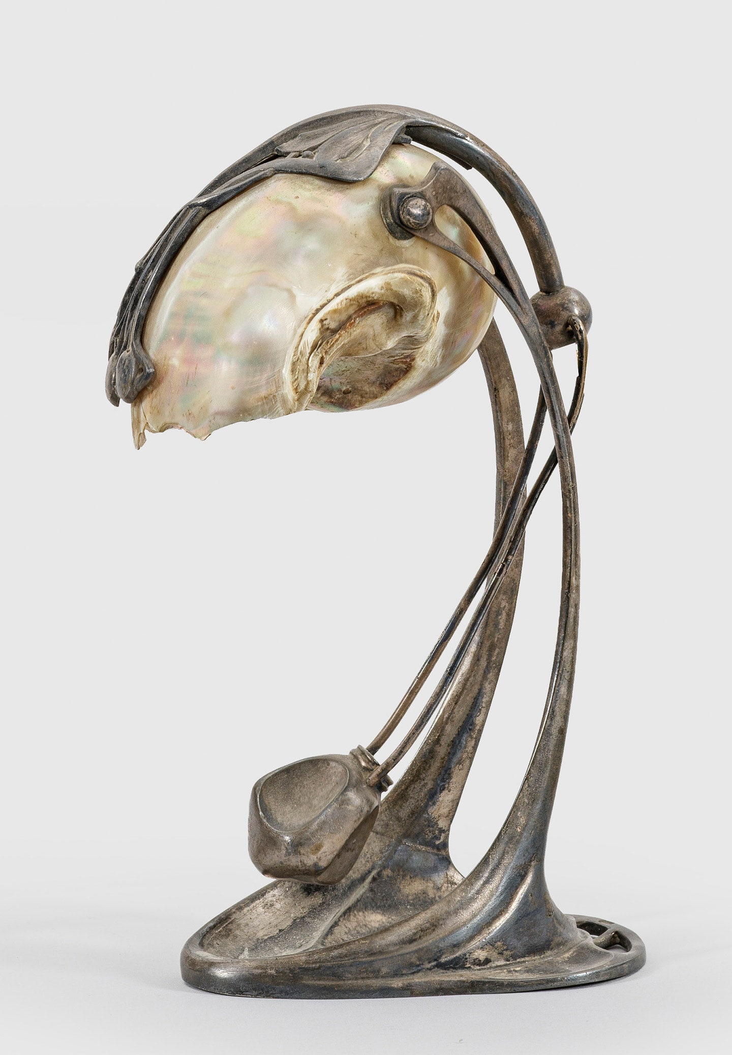 Jugendstil-Tischlampe von Moritz Hacker: 1-flg.; Metall, mit Resten von Versilberung und Gehäuse einer Nautilusmuschel. Vegetabil gestaltete Basis, in gebogte Streben übergehend. Dazwischen schwenkbares Leuchtmittel. Elektrifiziert. Besch.