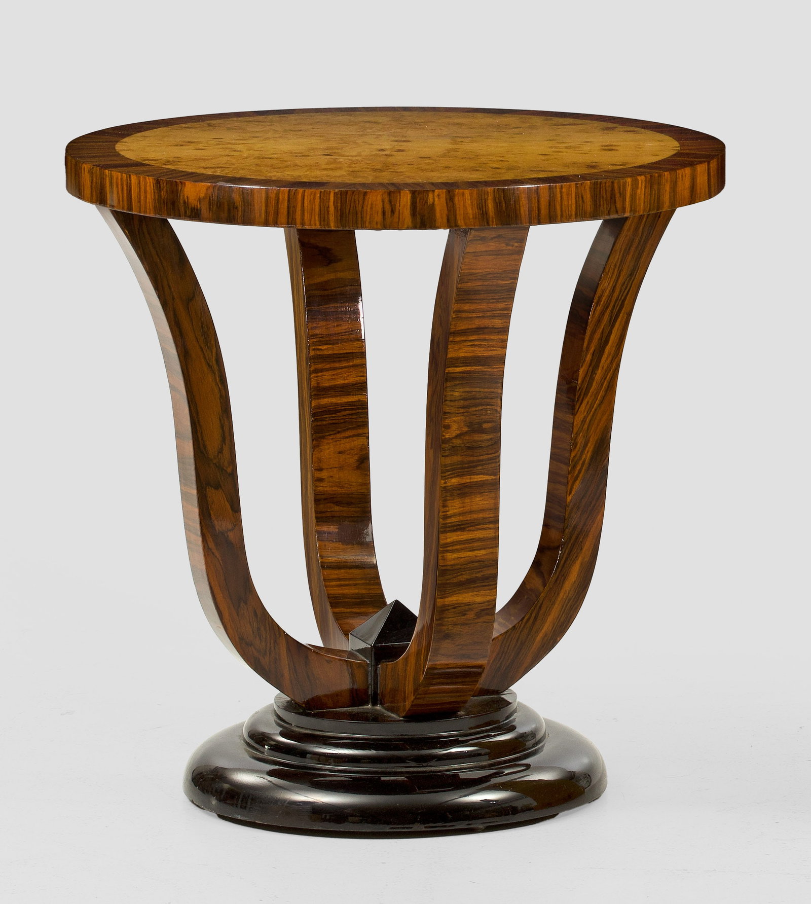 Beistelltisch im Art Déco-Stil: Nussbaum und Pappelmaser, furniert sowie teilw. ebonisiert. Über gestuft ansteigender Basis geschweifte Streben als Träger für runde Deckplatte. H. 59 cm. D. 60 cm. A French walnut and poplar wood 