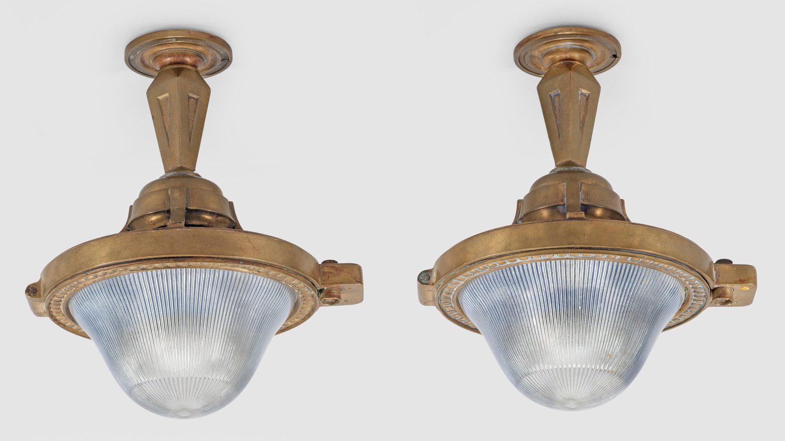 Paar Eisenbahnwagon-Deckenlampen: 1-flg.; Bronze sowie farbloses und blaues Glas. Balusterförmiger Korpus mit breitem Reif als Träger für reliefierte, bombierte Glaseinsätze. Oberhalb gekanteter Schaft sowie rosettenförmiger ober