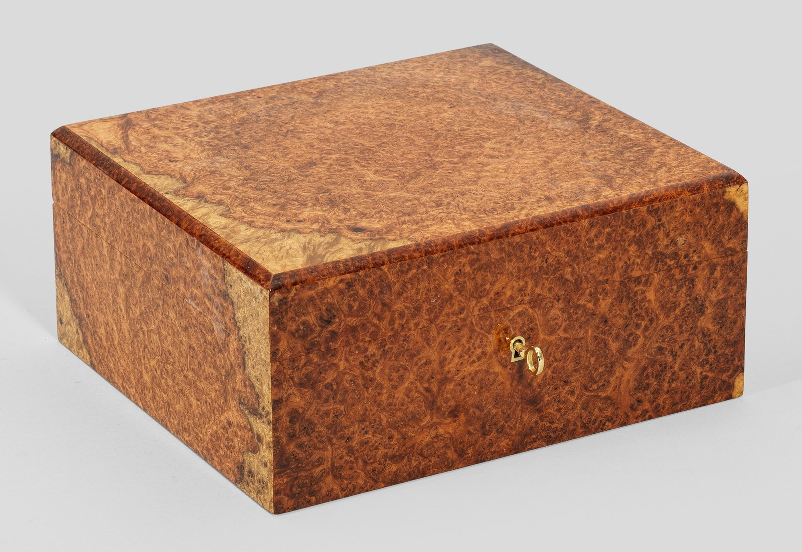 Humidor: Wurzelnuss, furniert. Gerader, rechteckig angelegter, abschließbarer Korpus mit entsprechendem, abgekantetem Flachdeckel. Innen Ablagefläche für Zigarren. Herstellerzeichen. H. 12,5 cm. 27,5 cm x 2