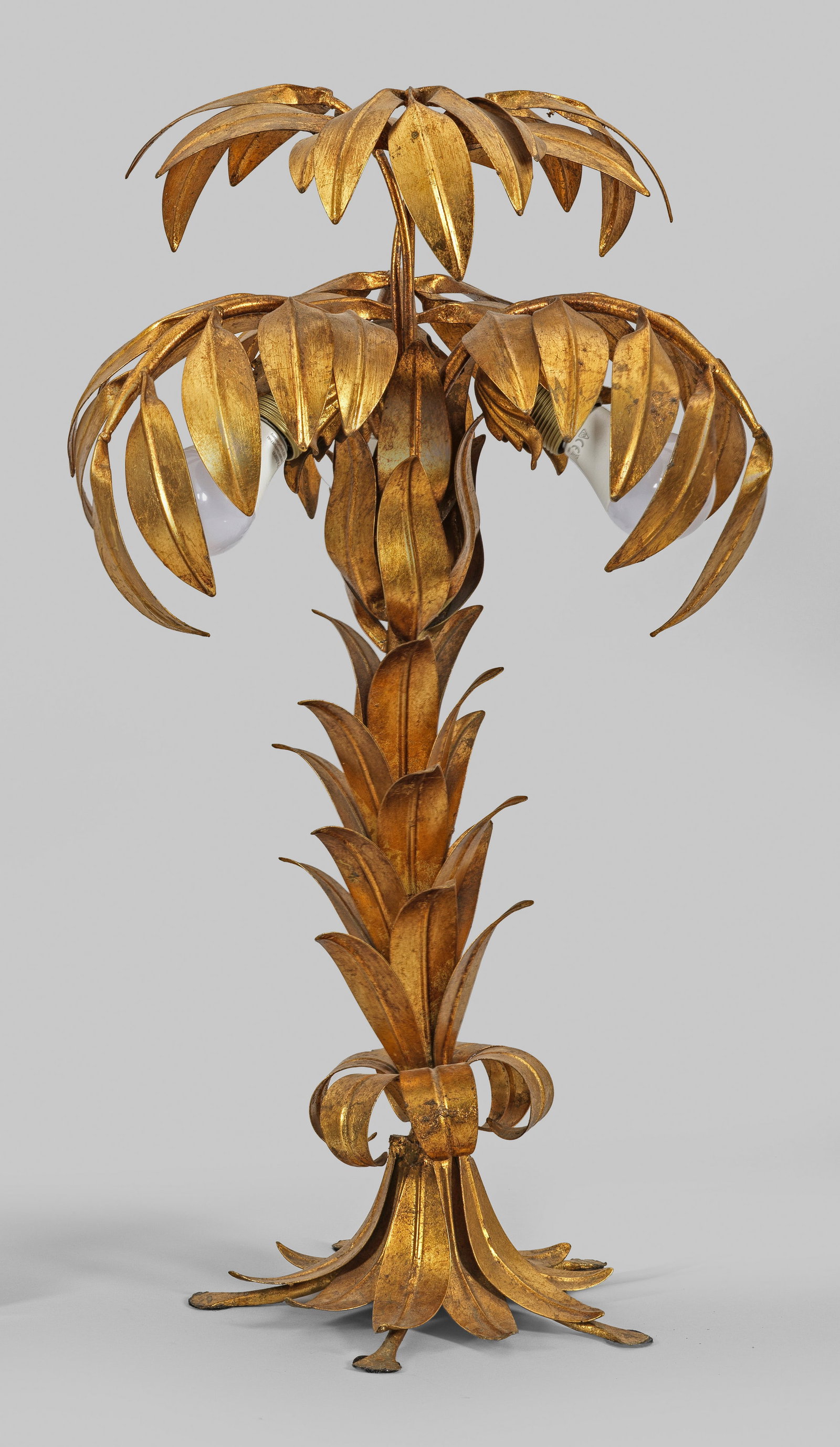 Hollywood Regency-Tischlampe: 3-flg.; Metall, vergoldet. Korpus aus üppigem Blattwerk in Form einer Palme mit gebogten Palmwedeln als Träger für Leuchtmittel. Unbez. Elektrifiziert. H. 66 cm. A German gilt metal Hollywood regen
