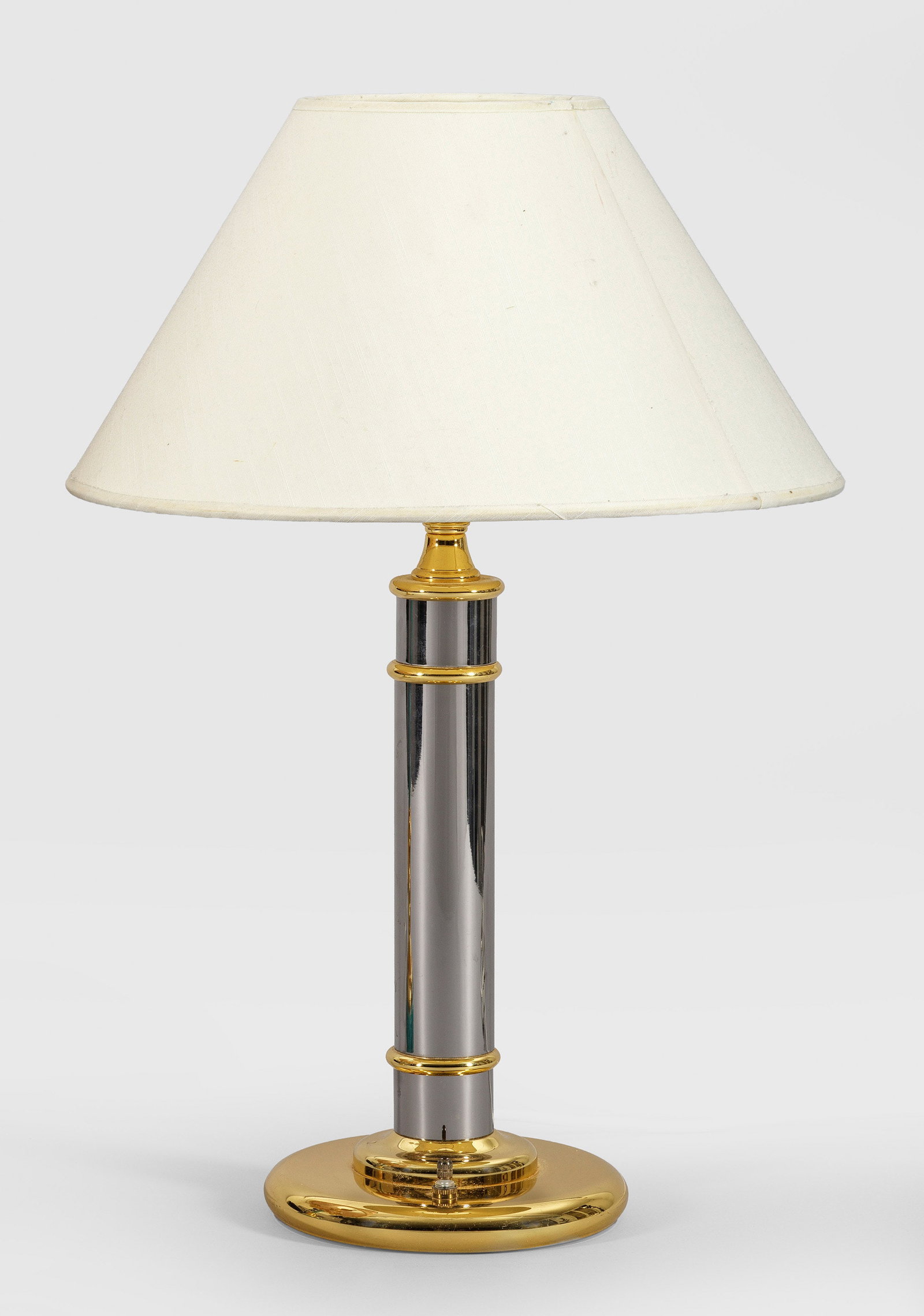 Dekorative Tischlampe: 1-flg.: Silber- und goldfarbenes Metall. Über runder Basis kräftiger Schaft als Träger für Leuchtmittel. Konischer Lampenschirm. Herstellerzeichen. Elektrifiziert. H. 56 cm. A decorative table lam