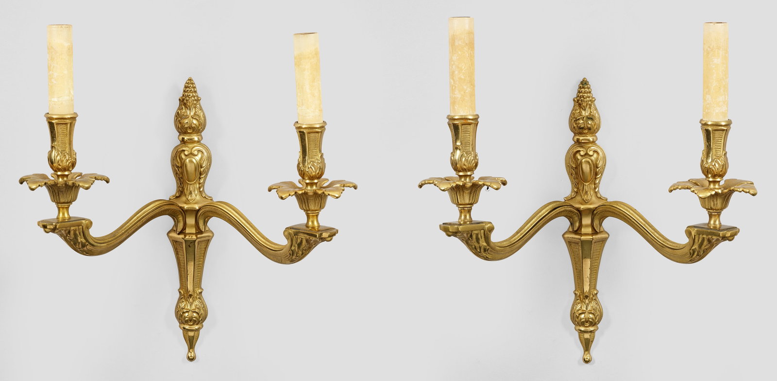 Paar Wandappliken: 2-flg.; Messing. Schmales, balusterförmiges Wandschild. Davon ausgehend stark geschwungene Leuchterarme mit vasenförmigen Tüllen über blattreliefierten Leuchterarmen. Elektrifiziert. H. 42 cm. A p