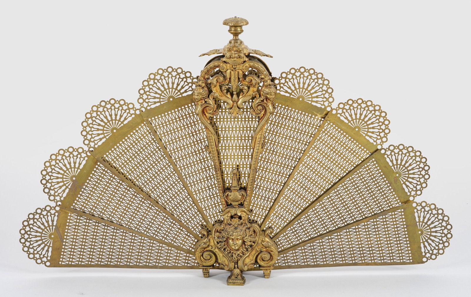 Napoleon III-Funkengitter: Bronze und Messing. Balusterförmiger, durchbrochen gearbeiteter Korpus aus üppigen Volutenmotiven mit Vasenbekrönung, flankiert von weiblichen Genien auf korrespondierender Basis mit zentralem Mask