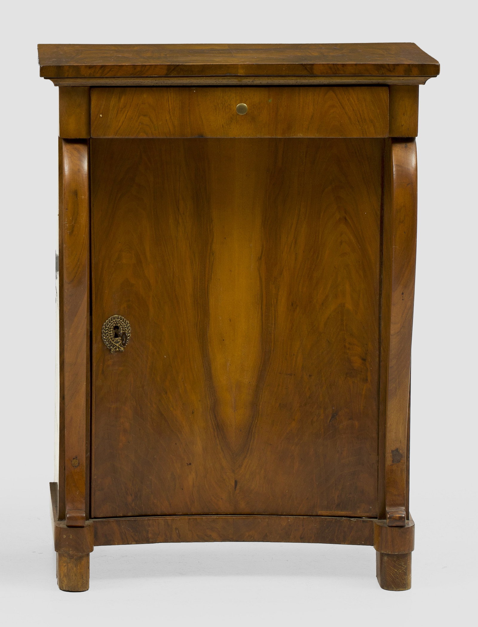 Biedermeier-Konsolschrank: Nussbaum, furniert. Gerader, hochrechteckiger Korpus auf schmaler Zarge und gerundeten Füßen. In der gegliederten Front konkav eingezogene Tür, flankiert von gestreckten Volutenmotiven als Stützen