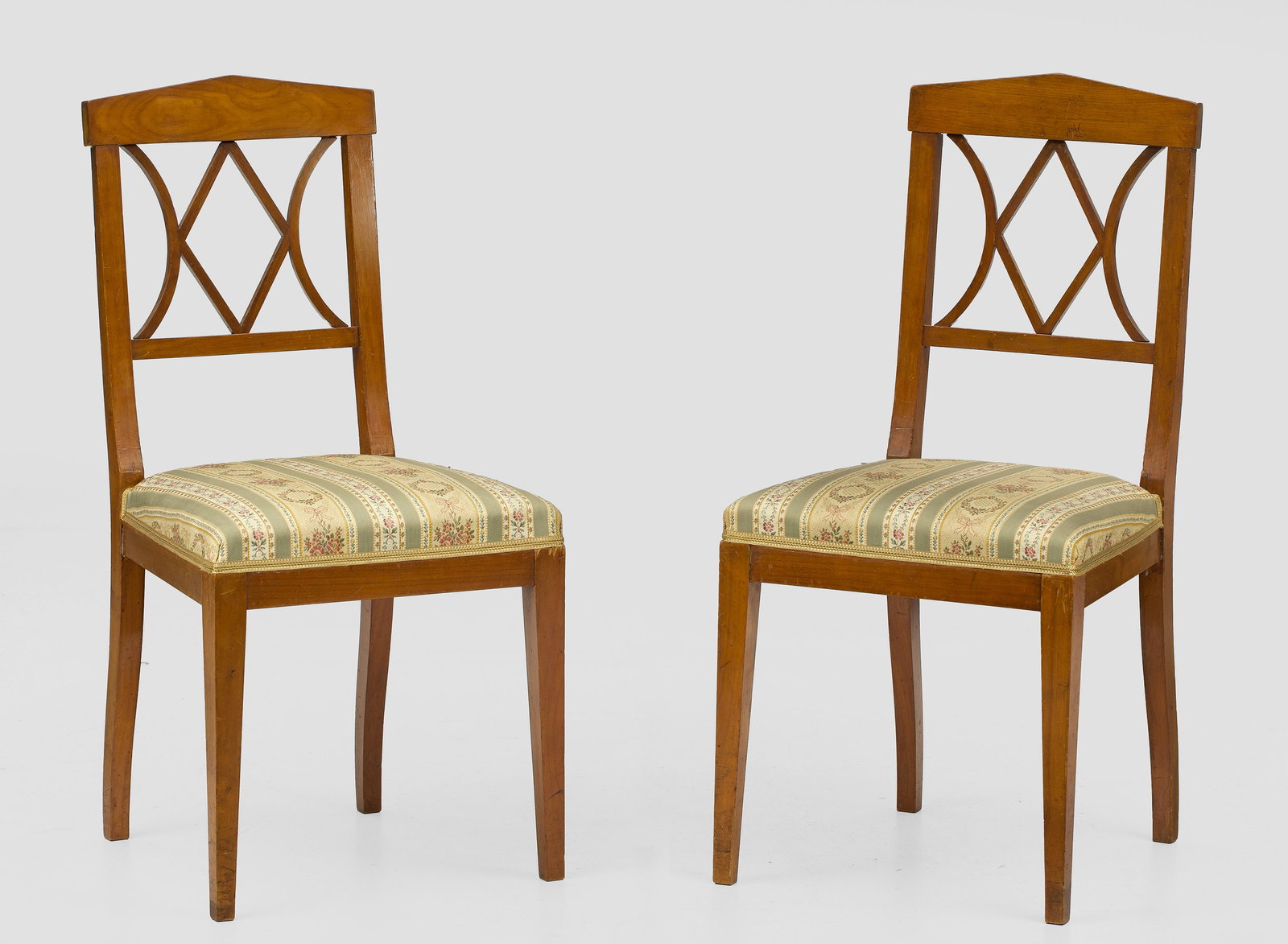 Paar Biedermeier-Stühle: Kirschbaum, furniert. Trapezförmige Zarge auf konischen Vierkantbeinen. Rechteckige, gitterartig durchbrochene Rückenlehnenrahmung mit dachartigem oberen Abschluss. Gepolstert und bezogen. Sitz-H. 4