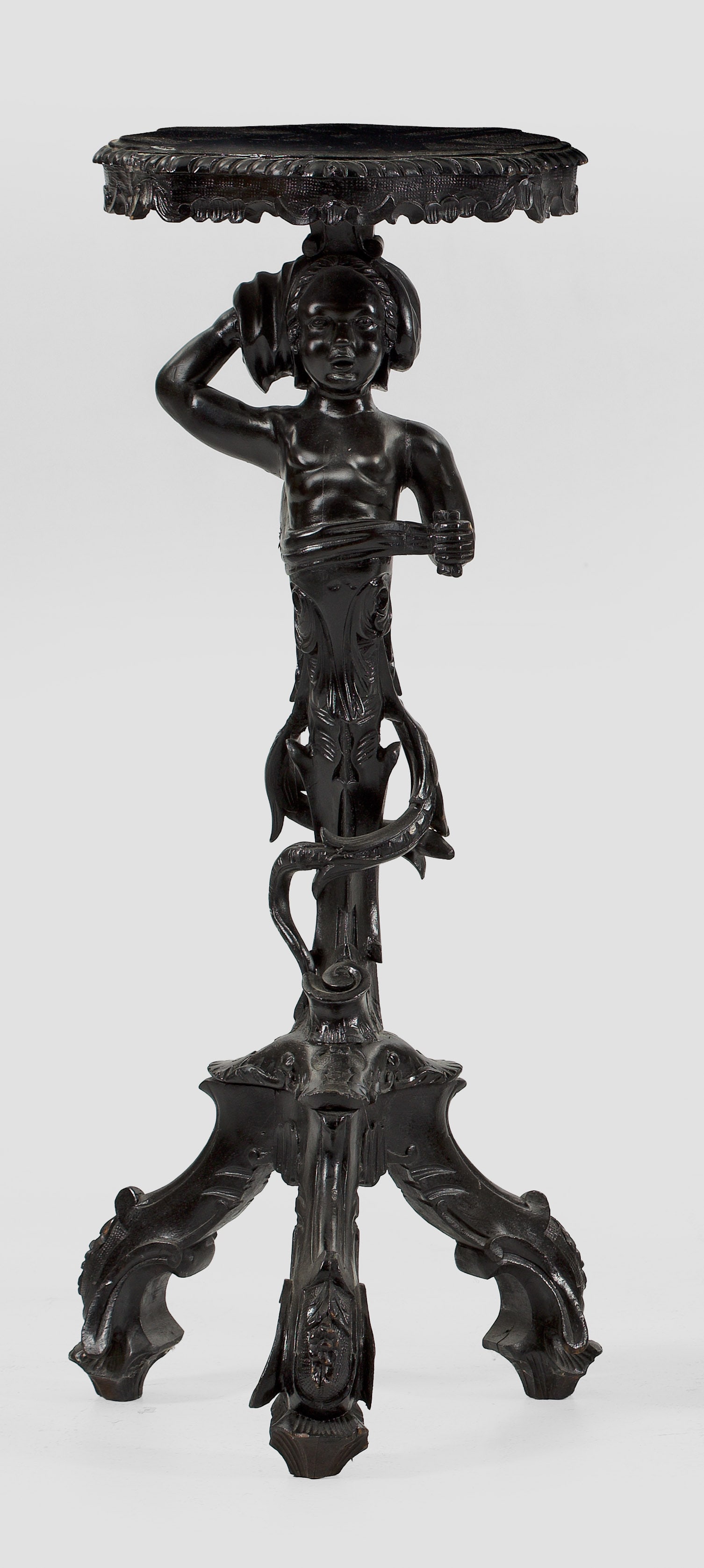 Belle Epoque-Gueridon: Holz, plastisch geschnitzt und schwarz lackiert. Skulptural gestalteter Schaft in Gestalt eines Genius auf Volutenbeinen als Träger für kartuschenförmige, profilierte Deckplatte. H. 96 cm. An Itali