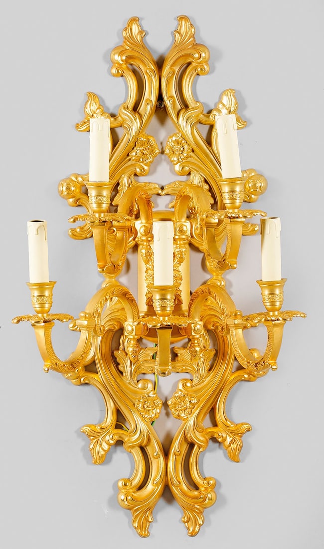 Große Wandapplike im Louis XIV-Stil: 5-flg.; Bronze, vergoldet. Durchbrochen gearbeitetes Wandschild aus üppigen, gegeneinander gesteckten Blattvoluten. Davon ausgehend stark geschwungene, gestaffelt angeordnete Leuchterarme mit vasenf�