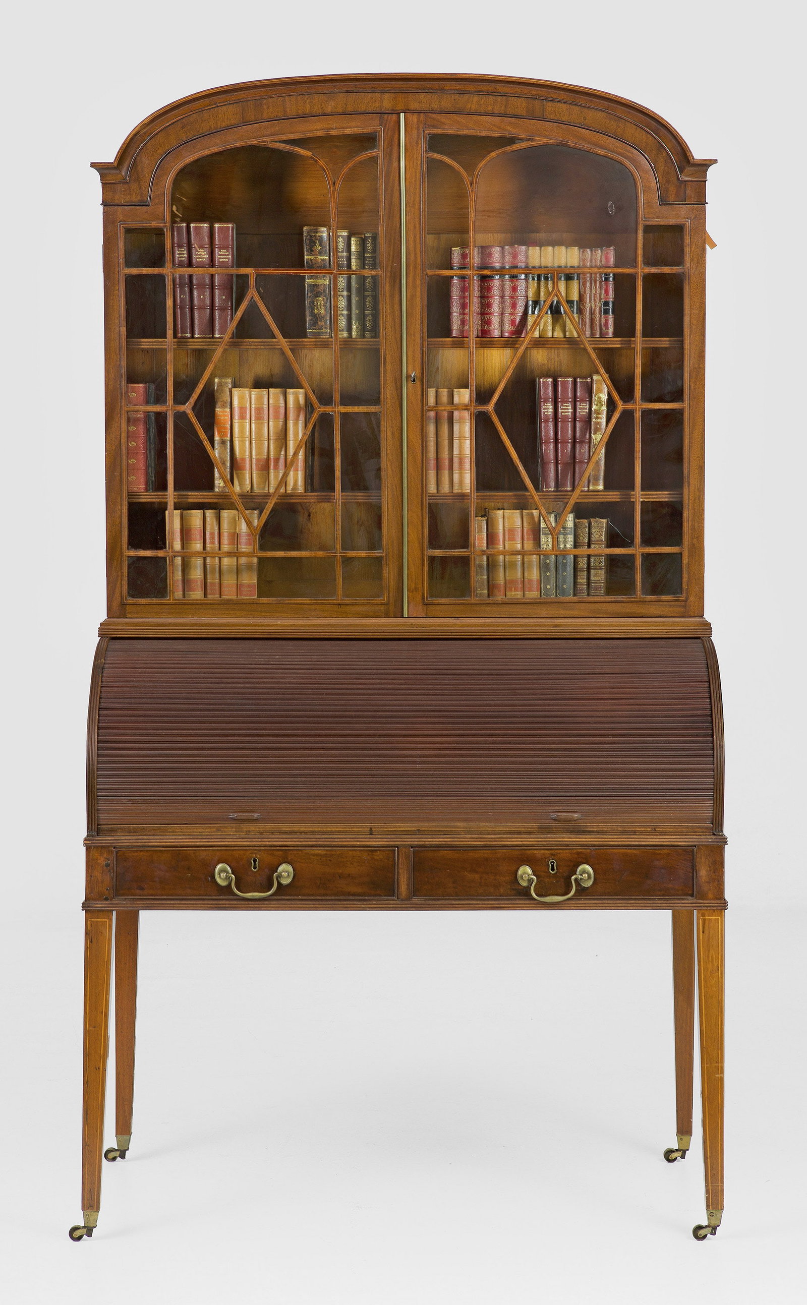 George III Secretaire Bookcase mit Rolloverschluss: Mahagoni. Gerader, zweischübiger Zargenkasten auf hohen, konischen Vierkantbeinen mit Messingrollen. Oberhalb bombierter Zylinderverschluss mit ausziehbarer, mit hellblauem Filz bespannter